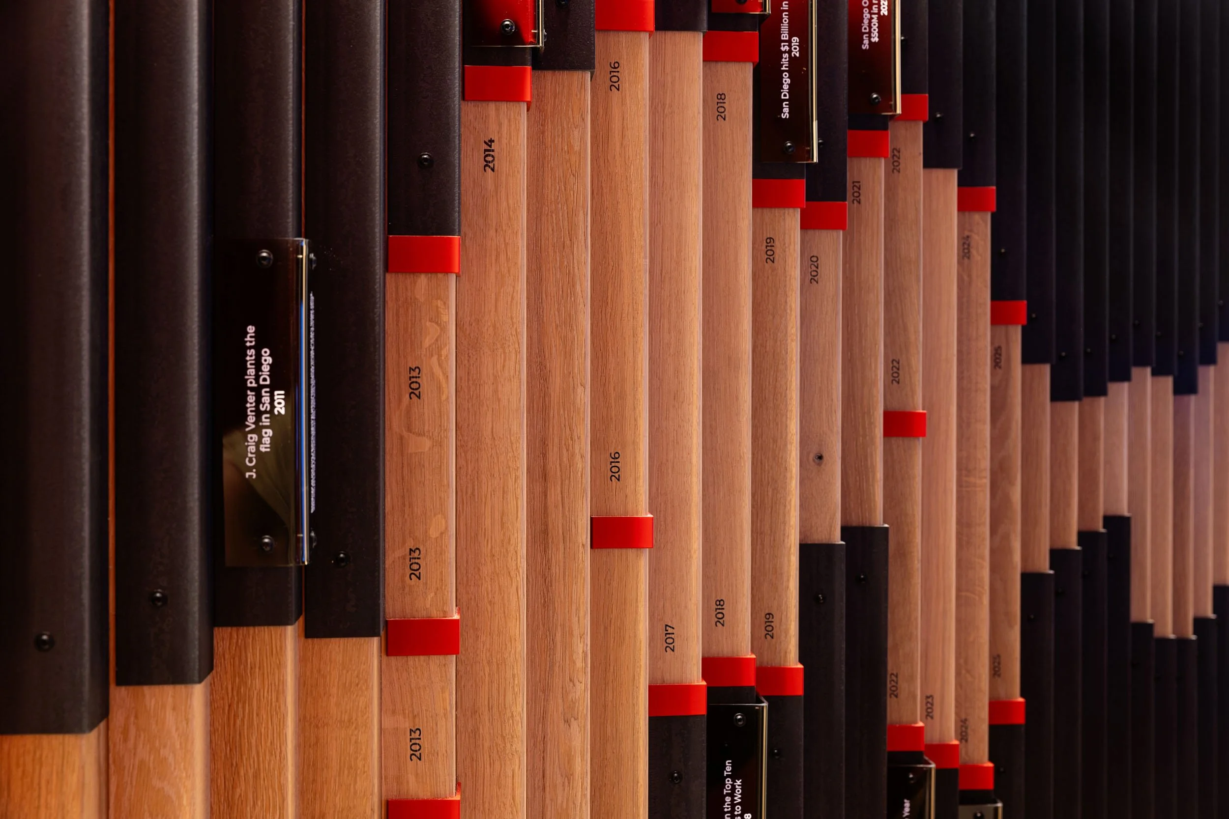 Vertical wood elements and red accents form a dimensional custom feature wall at the McCarthy office in San Diego.