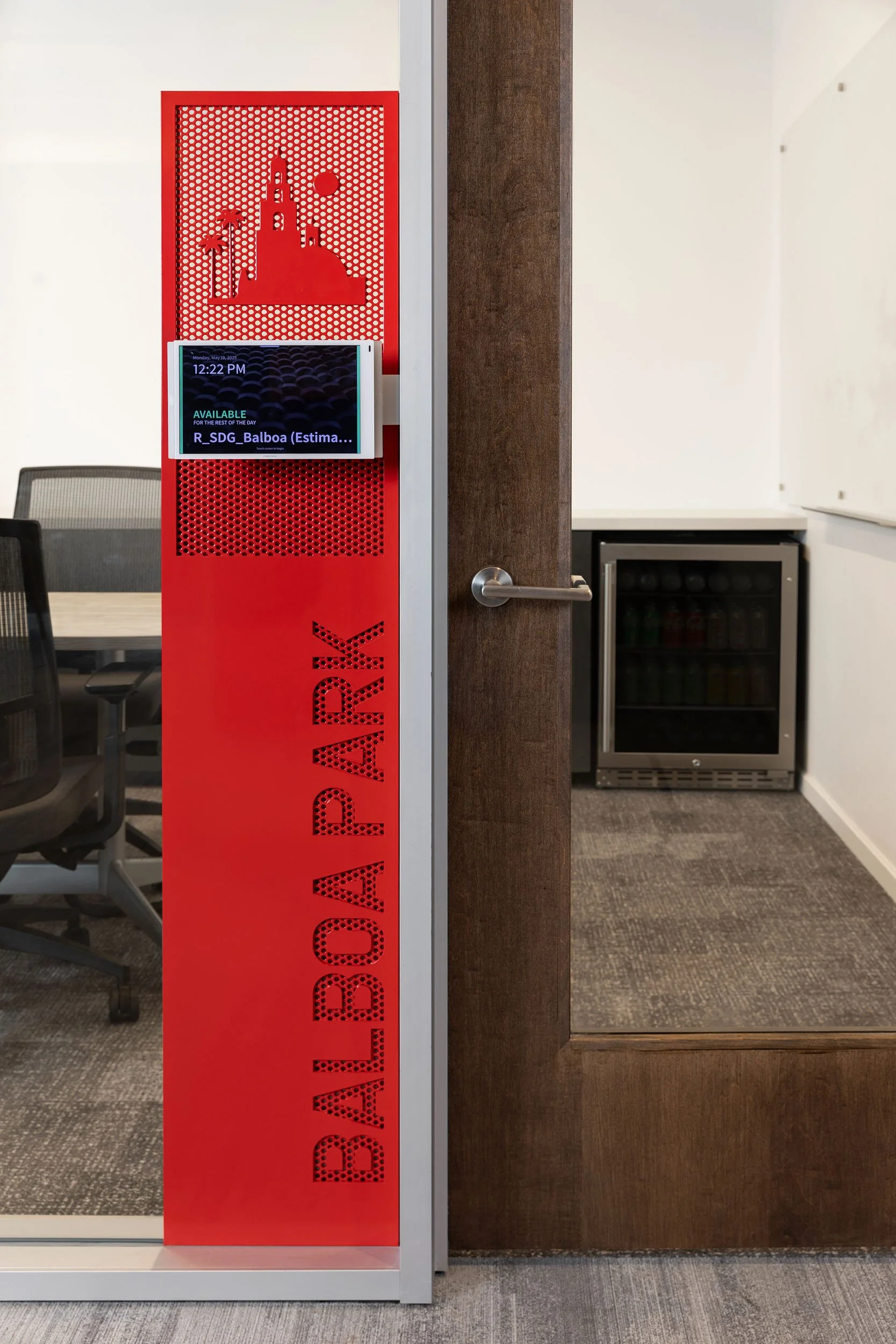 Red vertical Balboa Park wayfinding sign mounted beside an interior doorway at McCarthy office in San Diego.