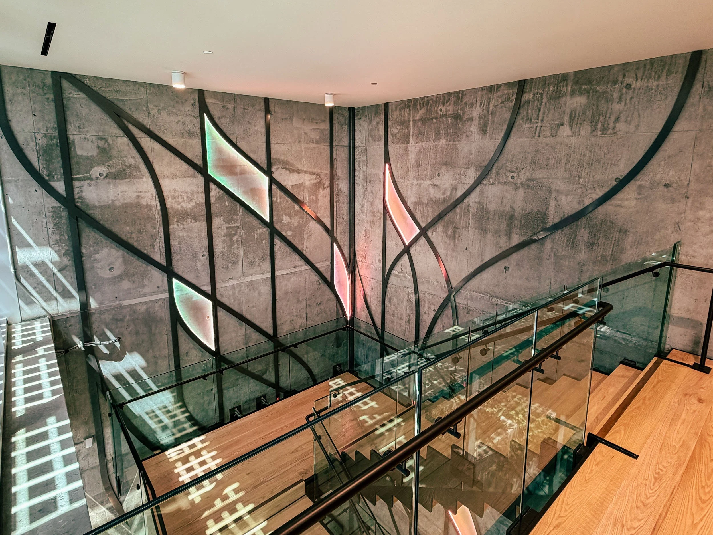 View from above a staircase surrounded by soft branching metal wall artwork and glass railings. 