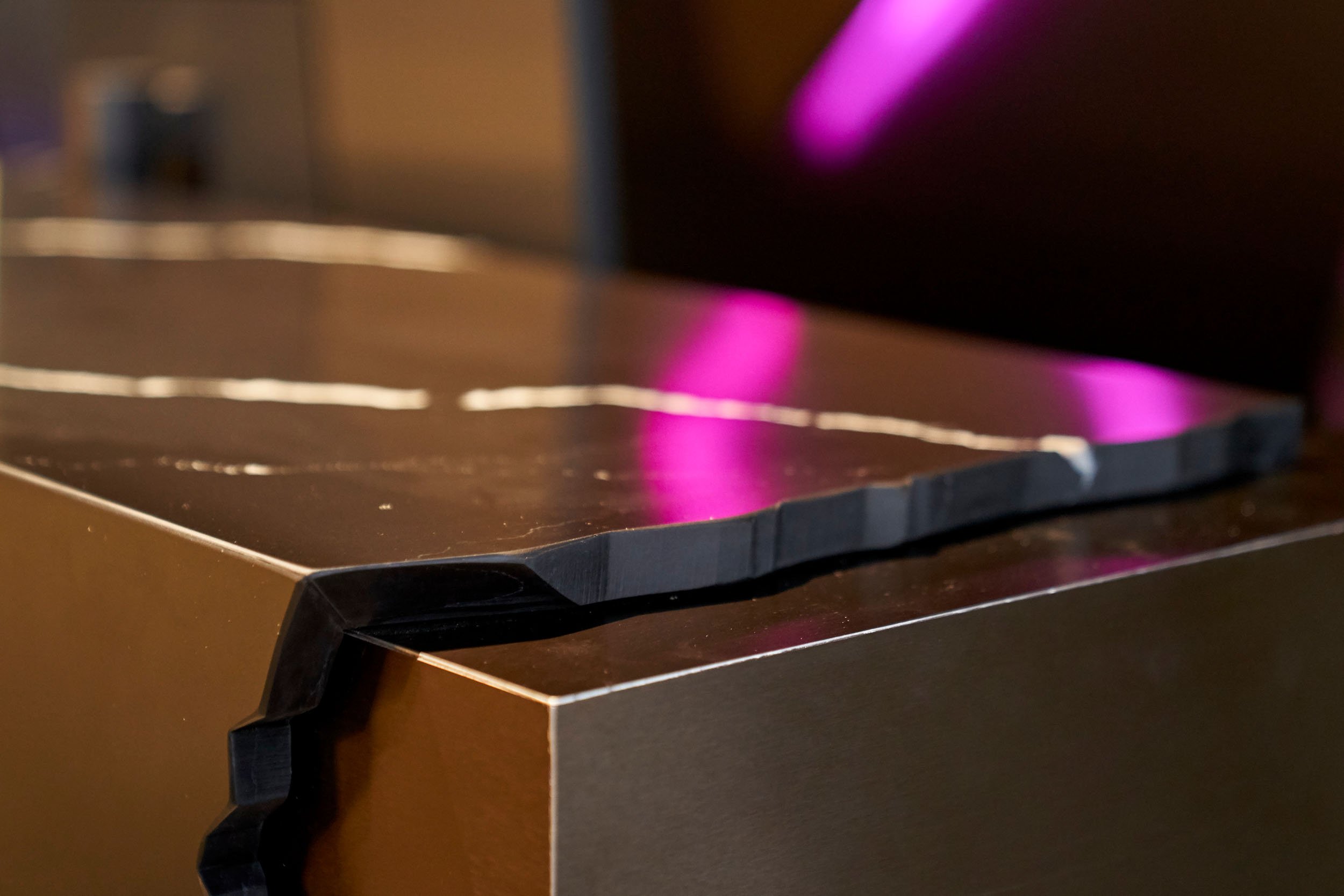 Dark custom lobby reception desk with rough cut stone on sleek brass.