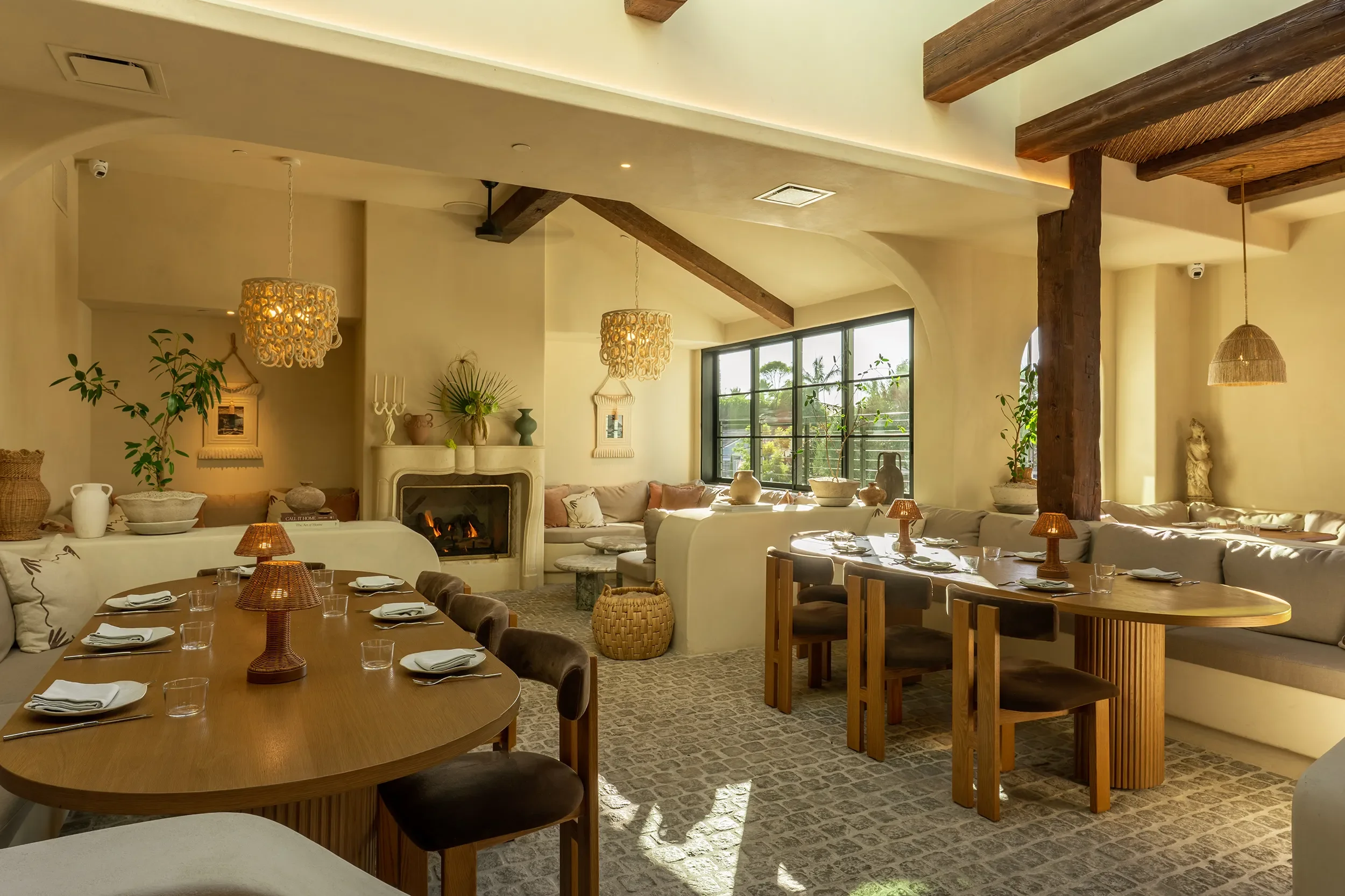 Fireplace dining room at By The Sea with built-in plaster seating, oval tables, and layered woven lighting