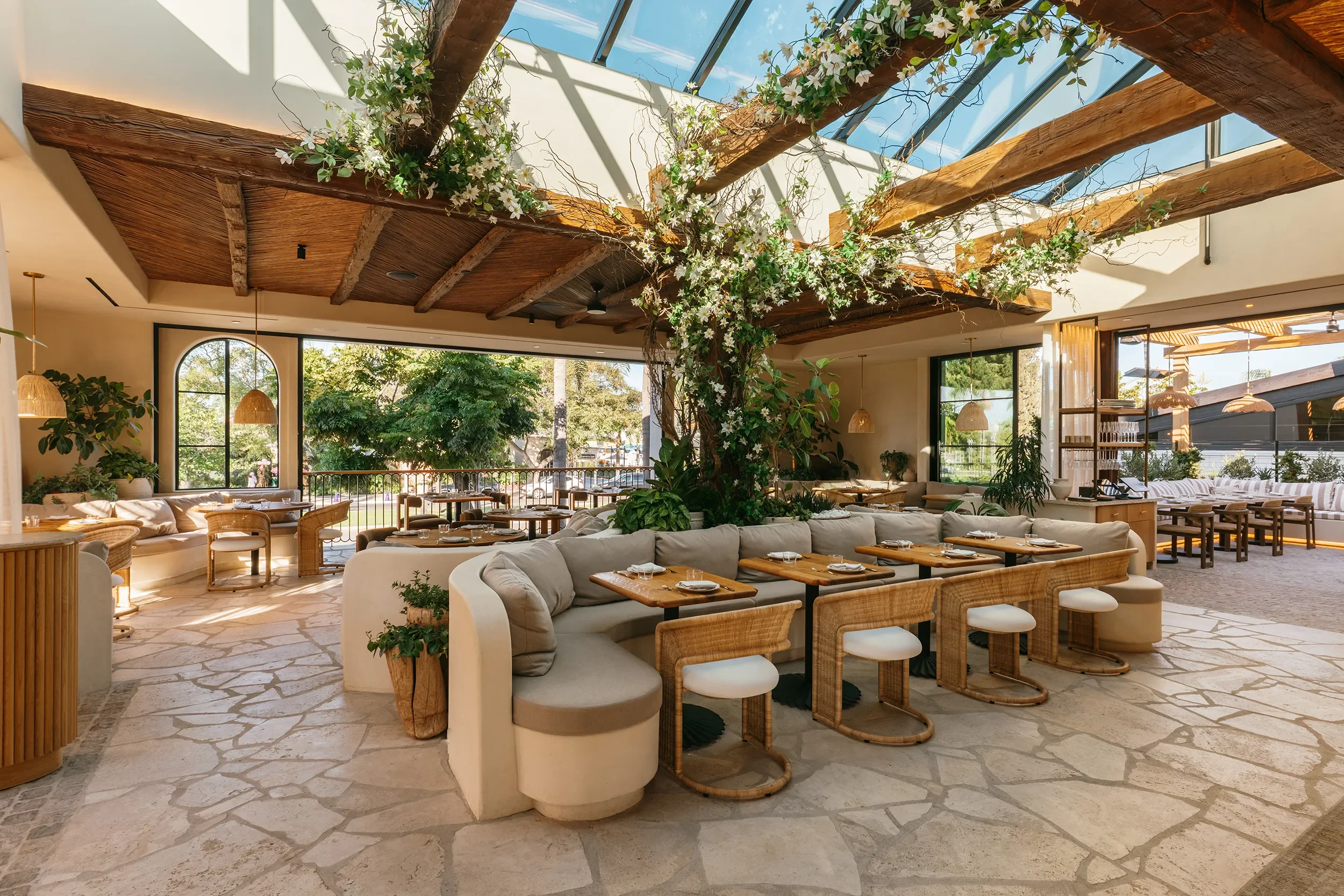 Skylit dining room with flagstone floors, curved banquettes, and a beamed pergola ceiling at By The Sea