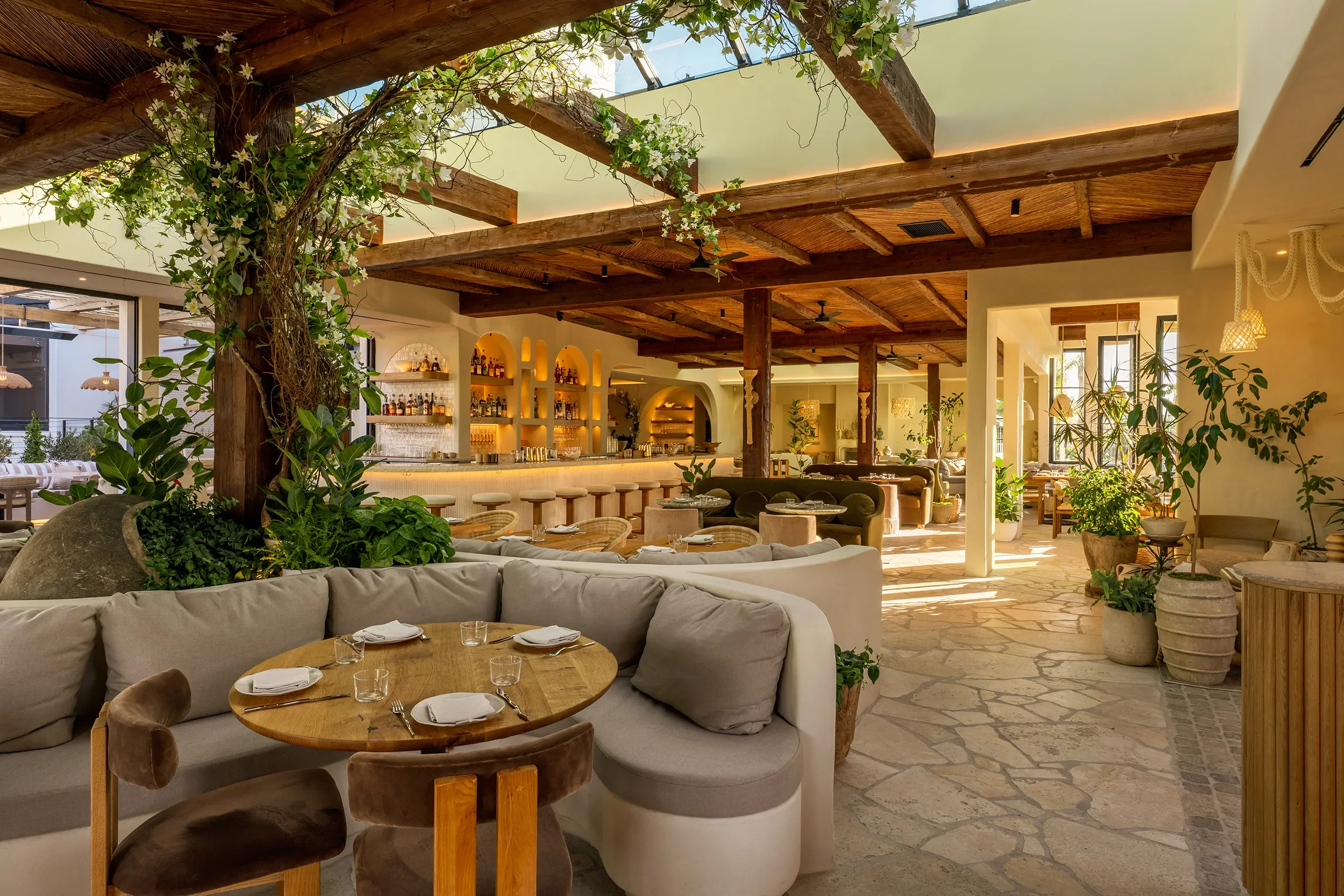 Preserved tree rising through the skylit dining room at By The Sea, with a curved banquette and round table