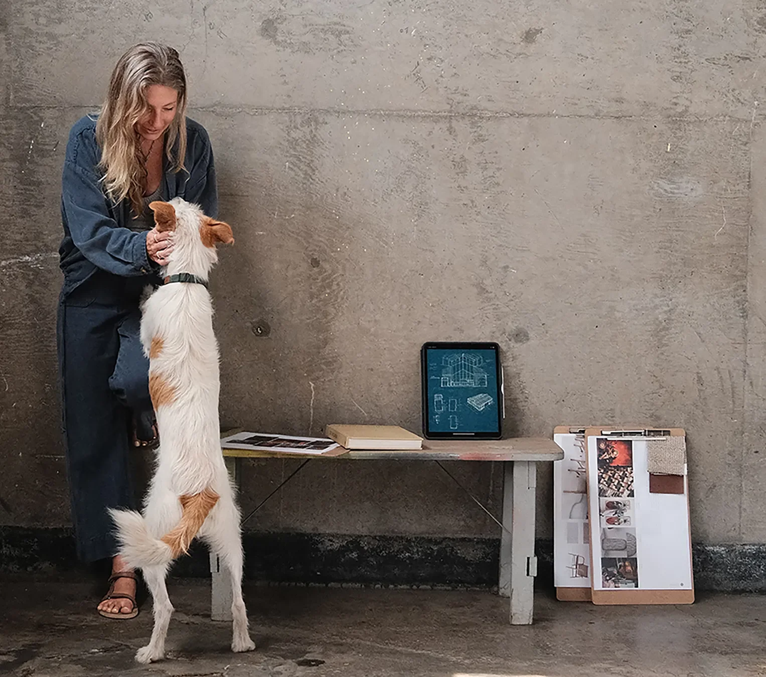 Tecture Studio designer with a shop dog beside a bench of material samples against a concrete wall.