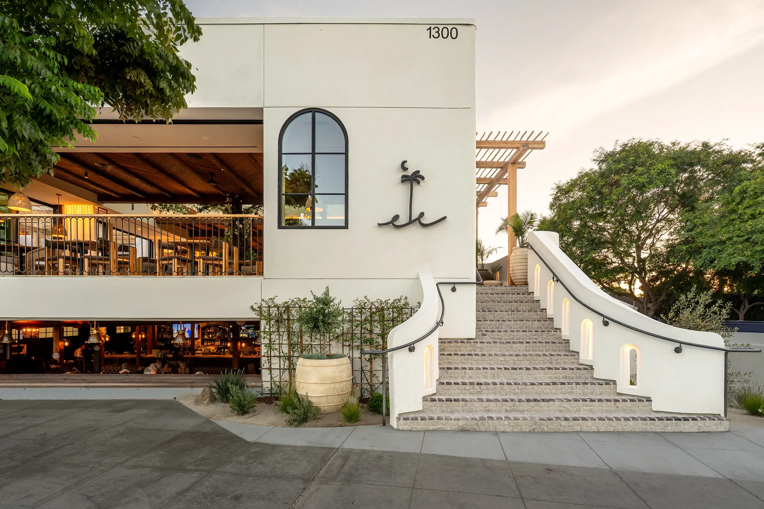 Arched window and anchor emblem on the white stucco facade of By The Sea, with lit steps at dusk