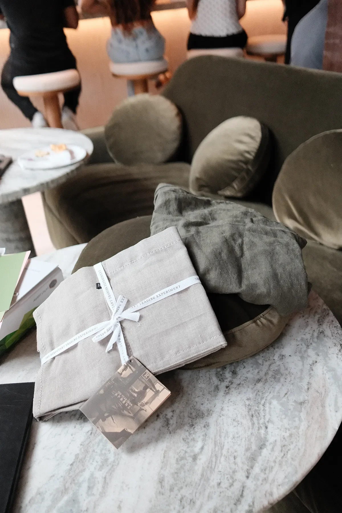 A folded linen sample on a marble side table beside the olive velvet lounge chairs at By The Sea