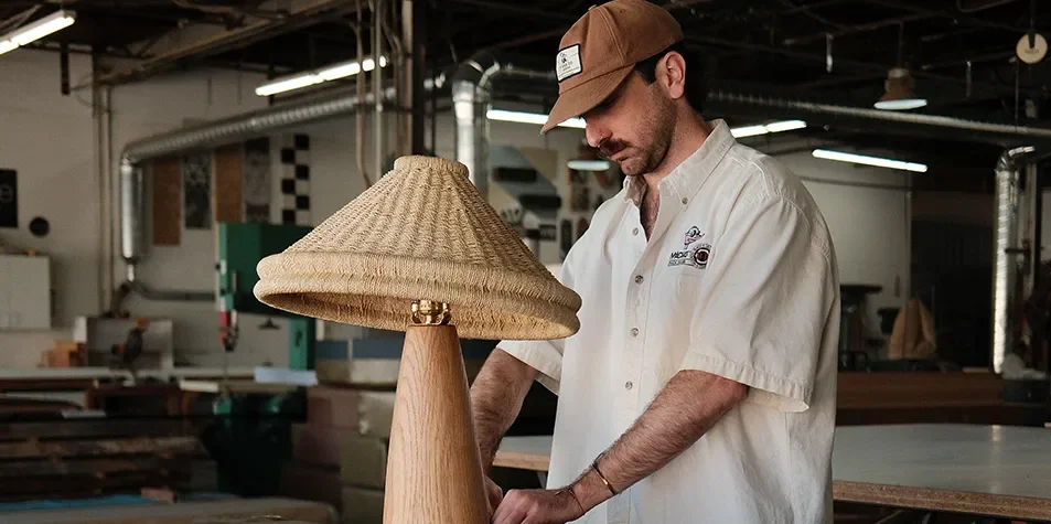 Tecture Studio designer inspecting a woven shade table lamp during a furniture quality check.