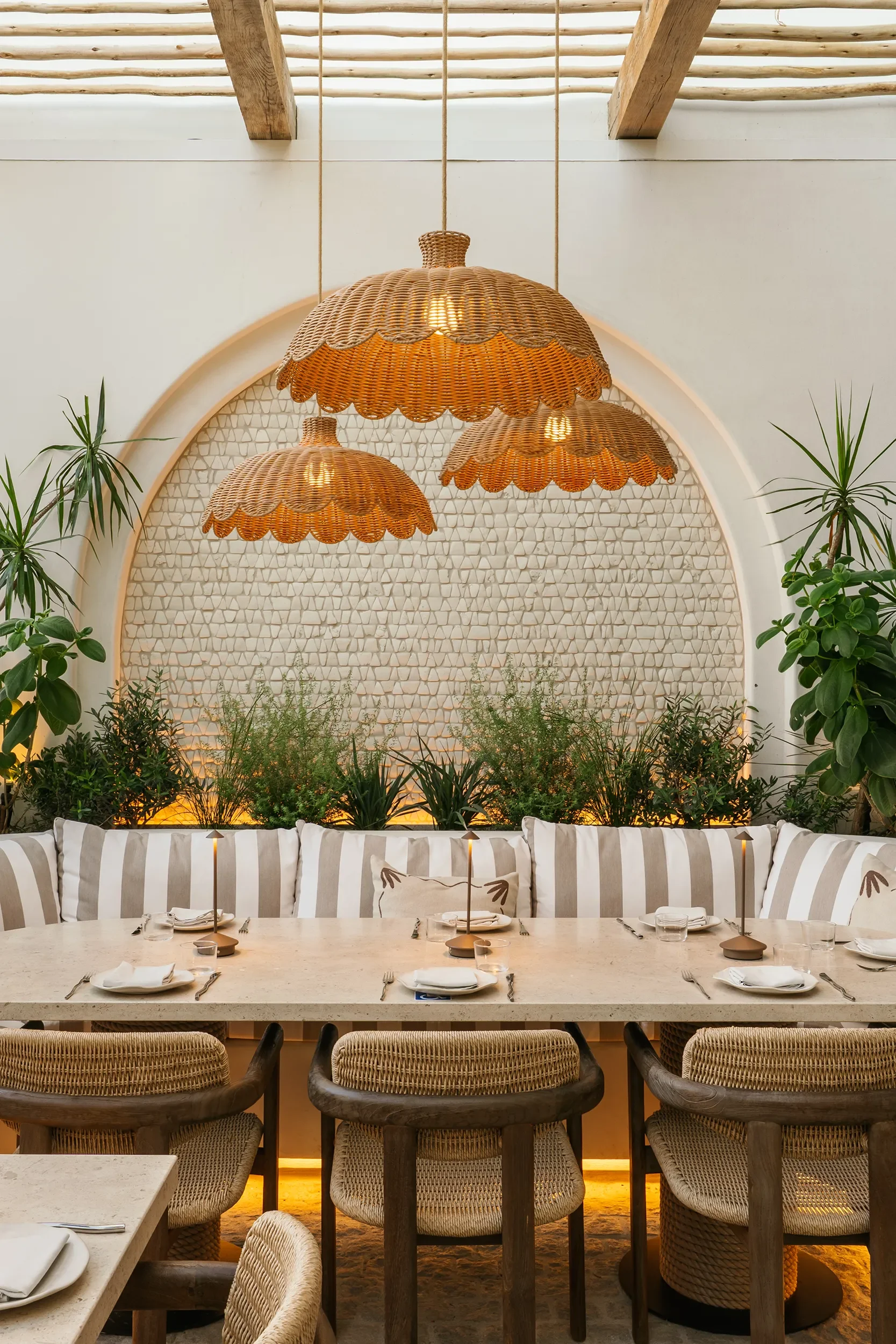 Scalloped rattan pendants over a striped banquette set into a whitewashed brick arch on the By The Sea patio terrace