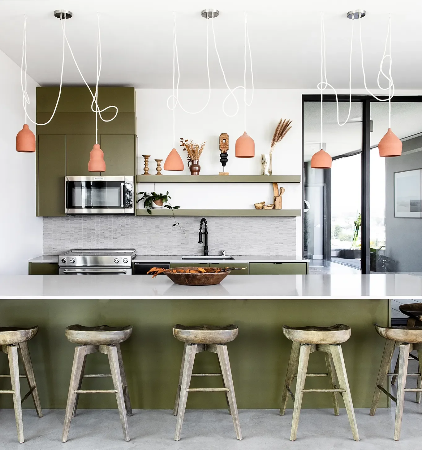 8th & B multifamily amenity kitchen interior with a green cabinetry, white counter, stools, and pendant lights.