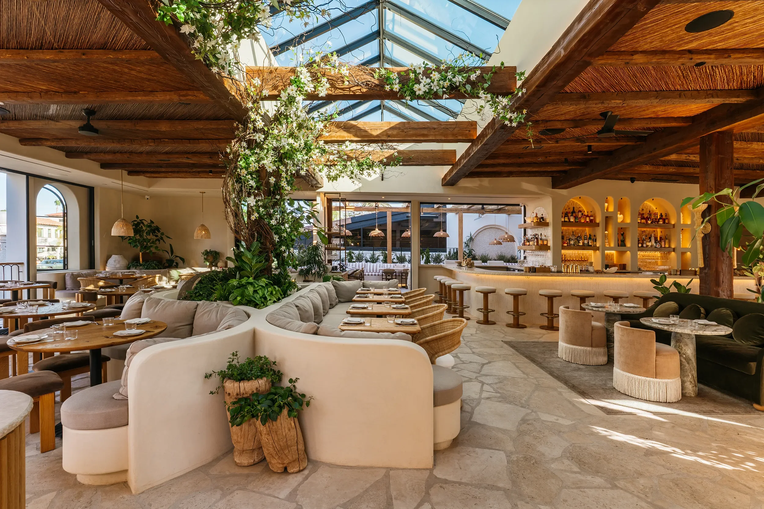 Skylit atrium lounge at By The Sea in Coronado with curved cream banquettes, climbing vines, and reclaimed beams