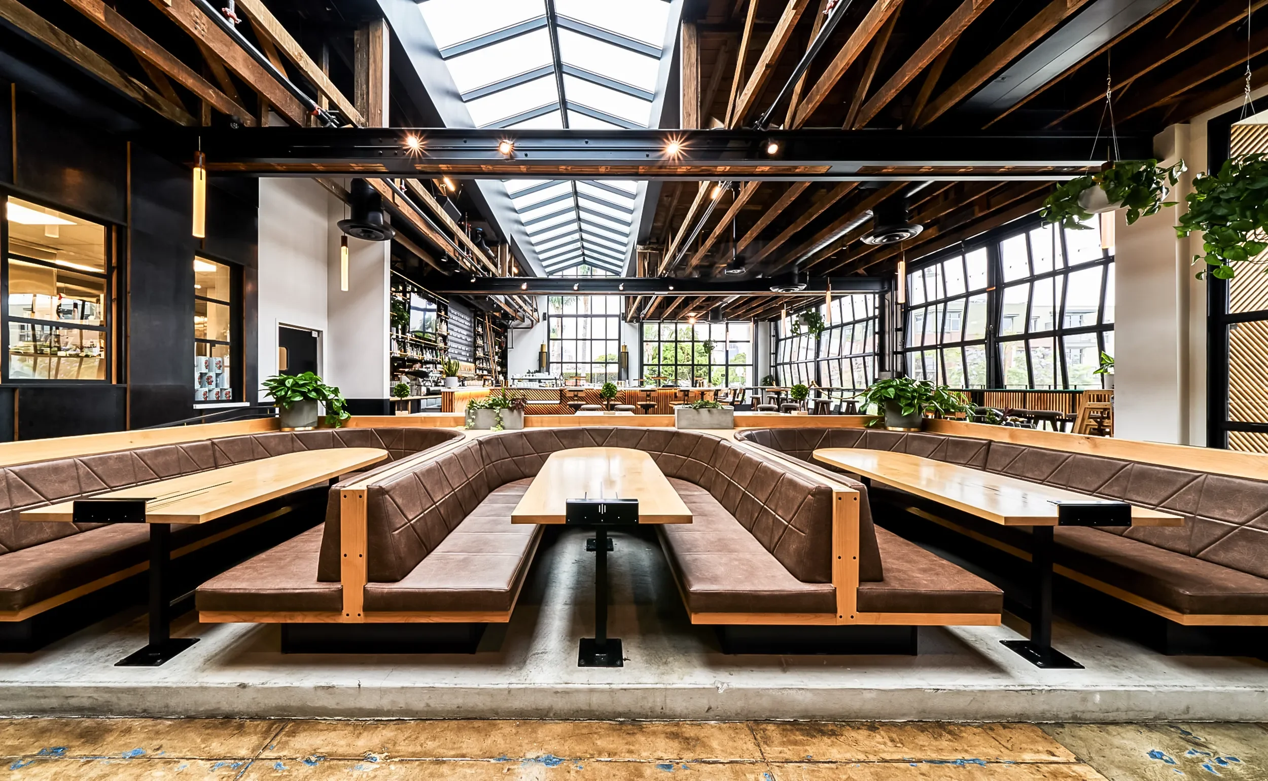 Long communal booths beneath the skylight and exposed redwood framing at Nolita Hall, Little Italy