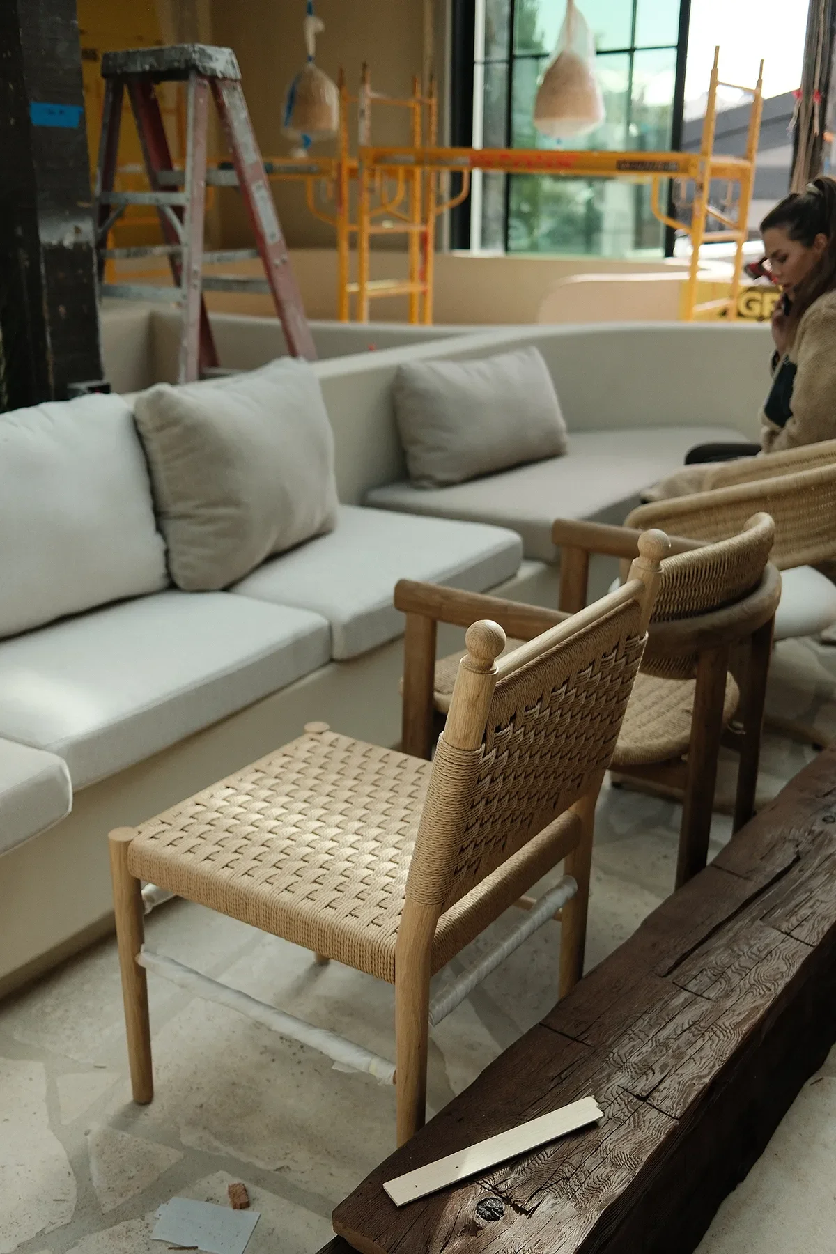 Woven-seat oak chairs set against the plaster banquette while scaffolding is still up at By The Sea