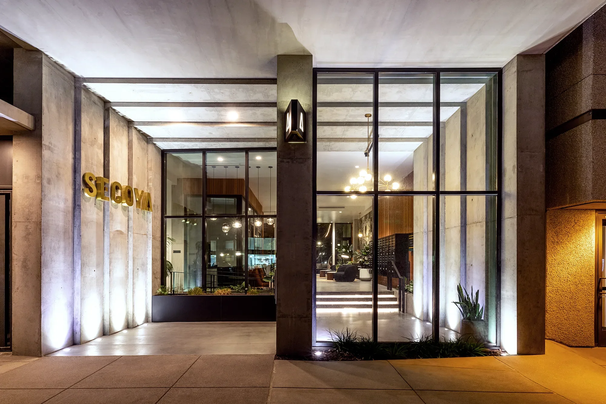 Illuminated entry at Secoya By The Park in San Diego with brass signage and glass facade.