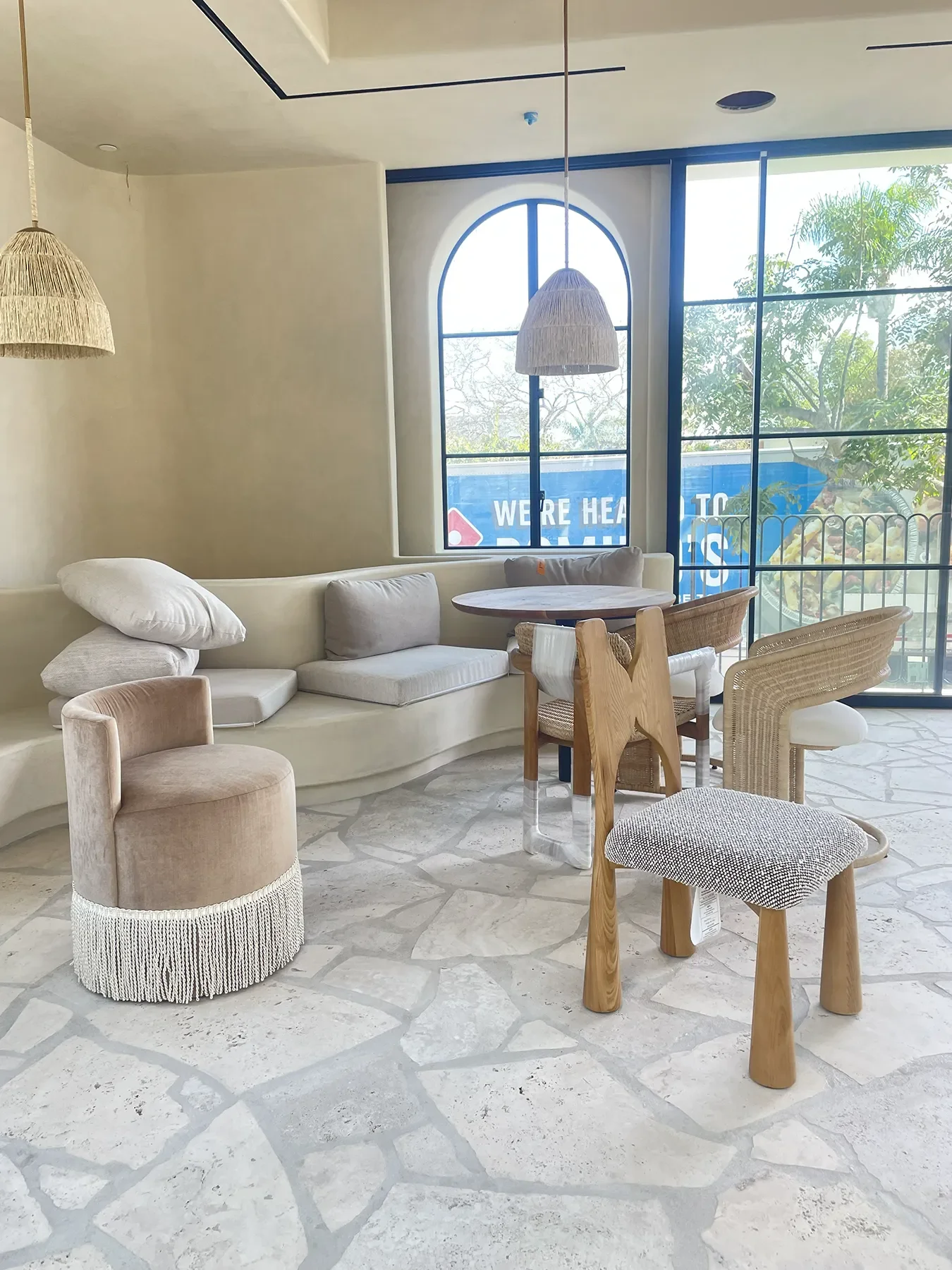 A fringed velvet swivel chair and sculptural oak stool in the window corner at B The Sea, Coronado