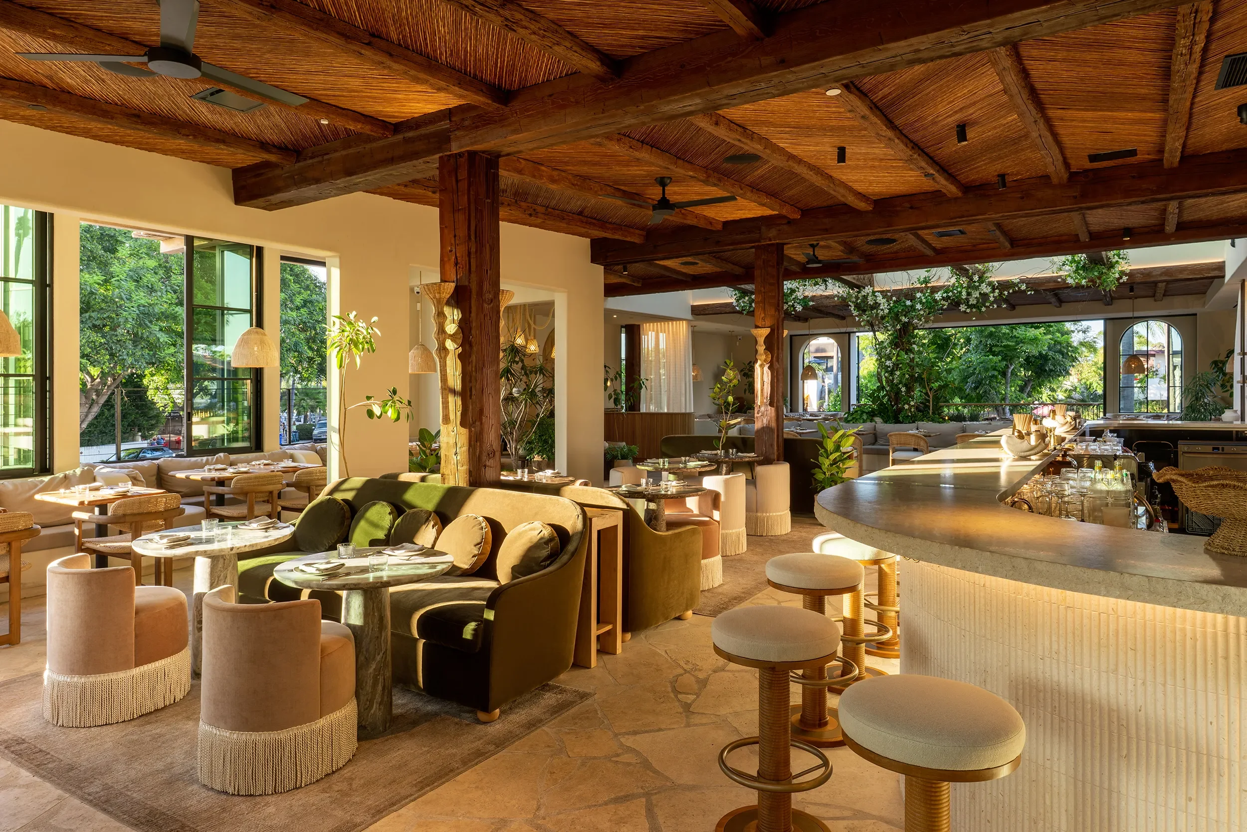 Green velvet armchairs and fringed ottomans in the lounge beside the curved bar at By The Sea