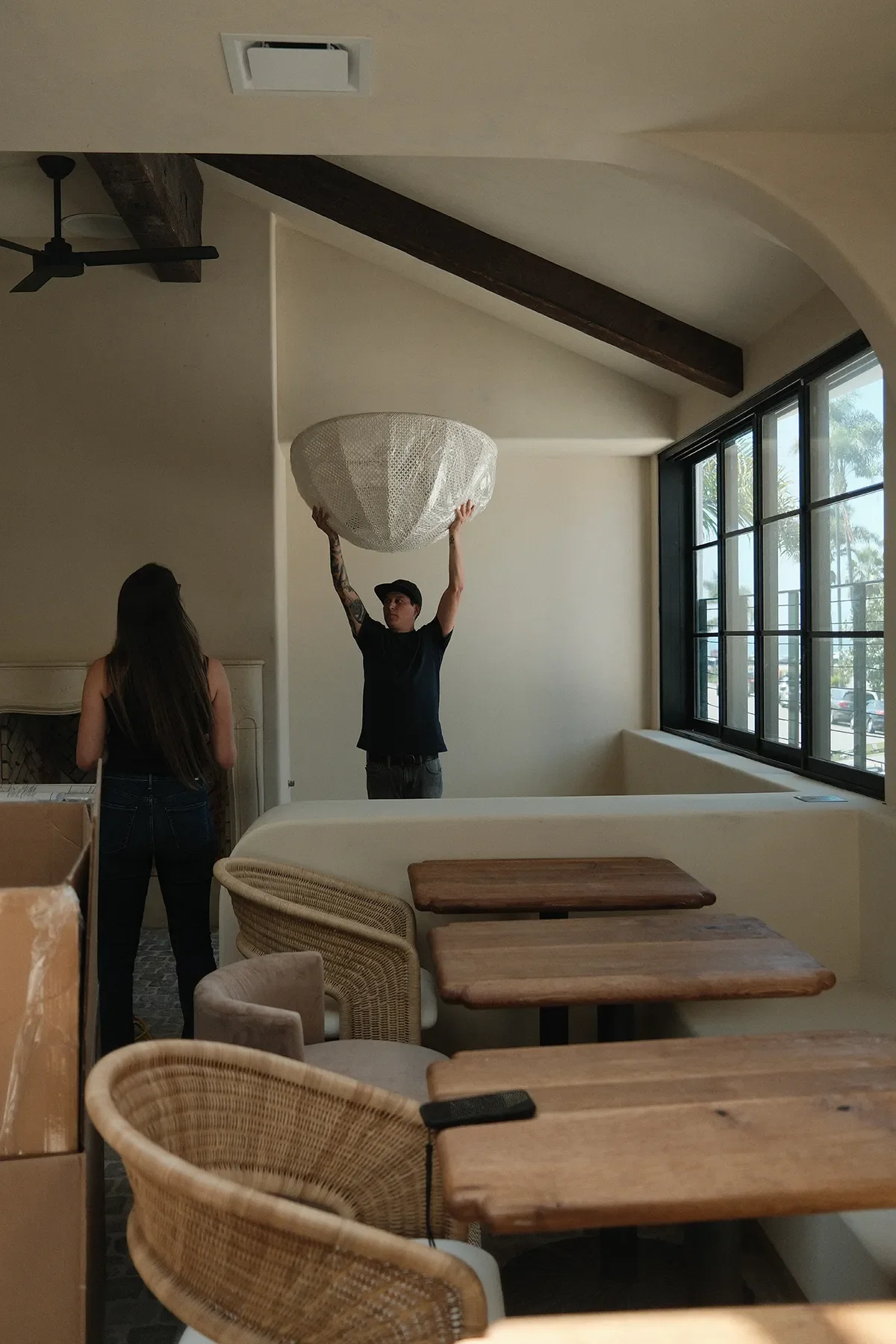 Man lifting a woven dome pendant into place above the banquette at By The Sea in Coronado