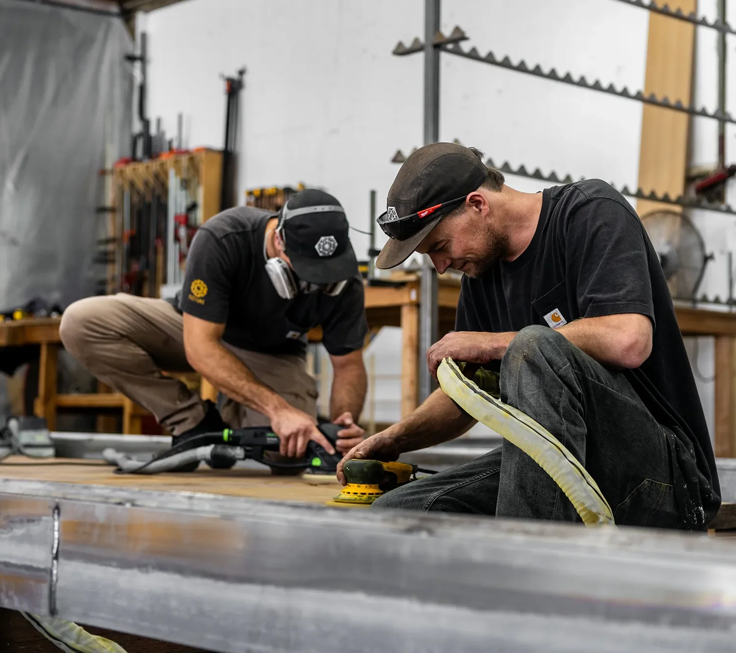 Two Tecture AF fabricators grinding a long curved metal track on the shop floor in San Diego