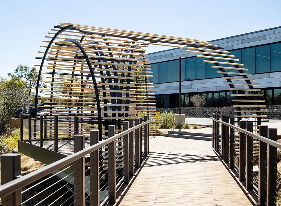 Arched steel and wood slat tunnel trellis over a boardwalk walkway on a Torrey Pines campus