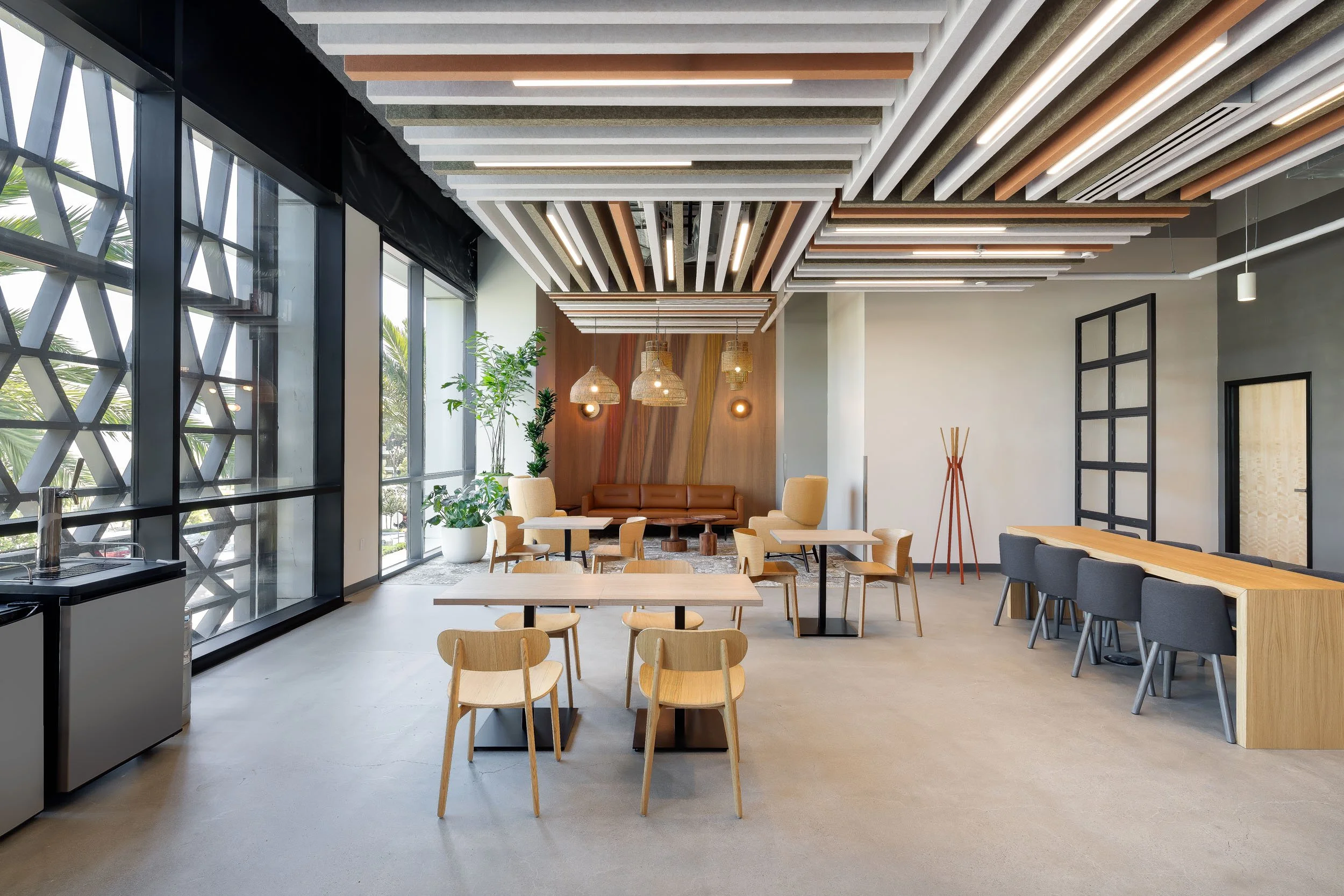 A corporate office break area with a lounge, small tables, and a communal table with a custom felt ceiling feature.