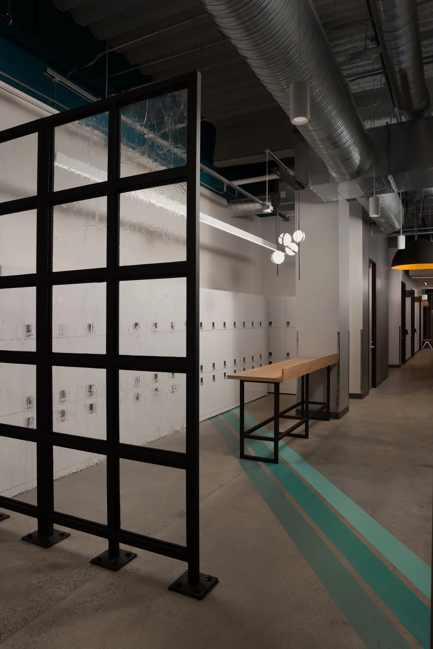 A corporate office locker area with a custom fabricated black-framed partition wall with a grid of textured glass panels, and a gradient blue floor graphic. 