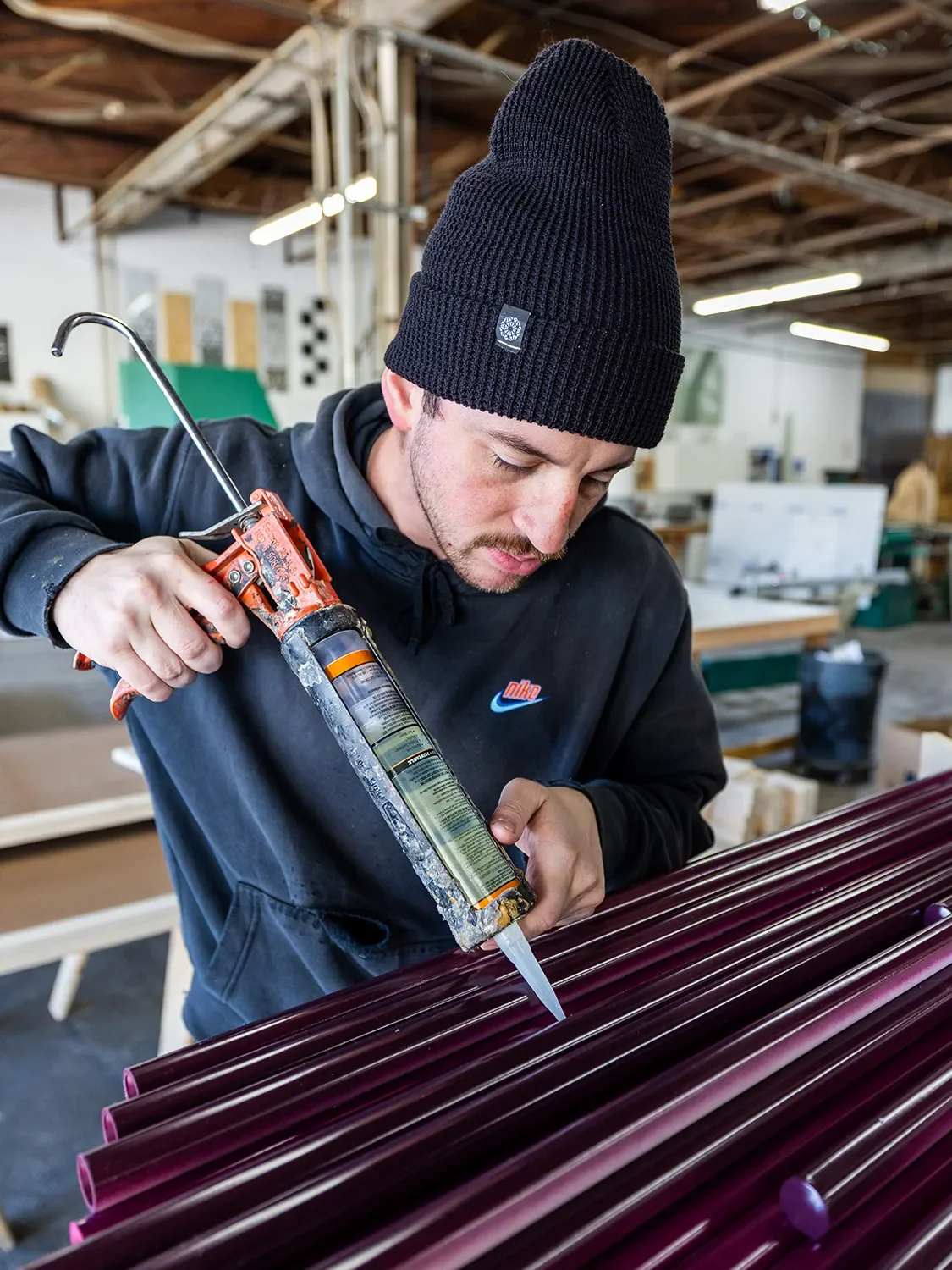 Isaac Rominger applying adhesive to a row of burgundy PVC pipes in the Tecture AF shop