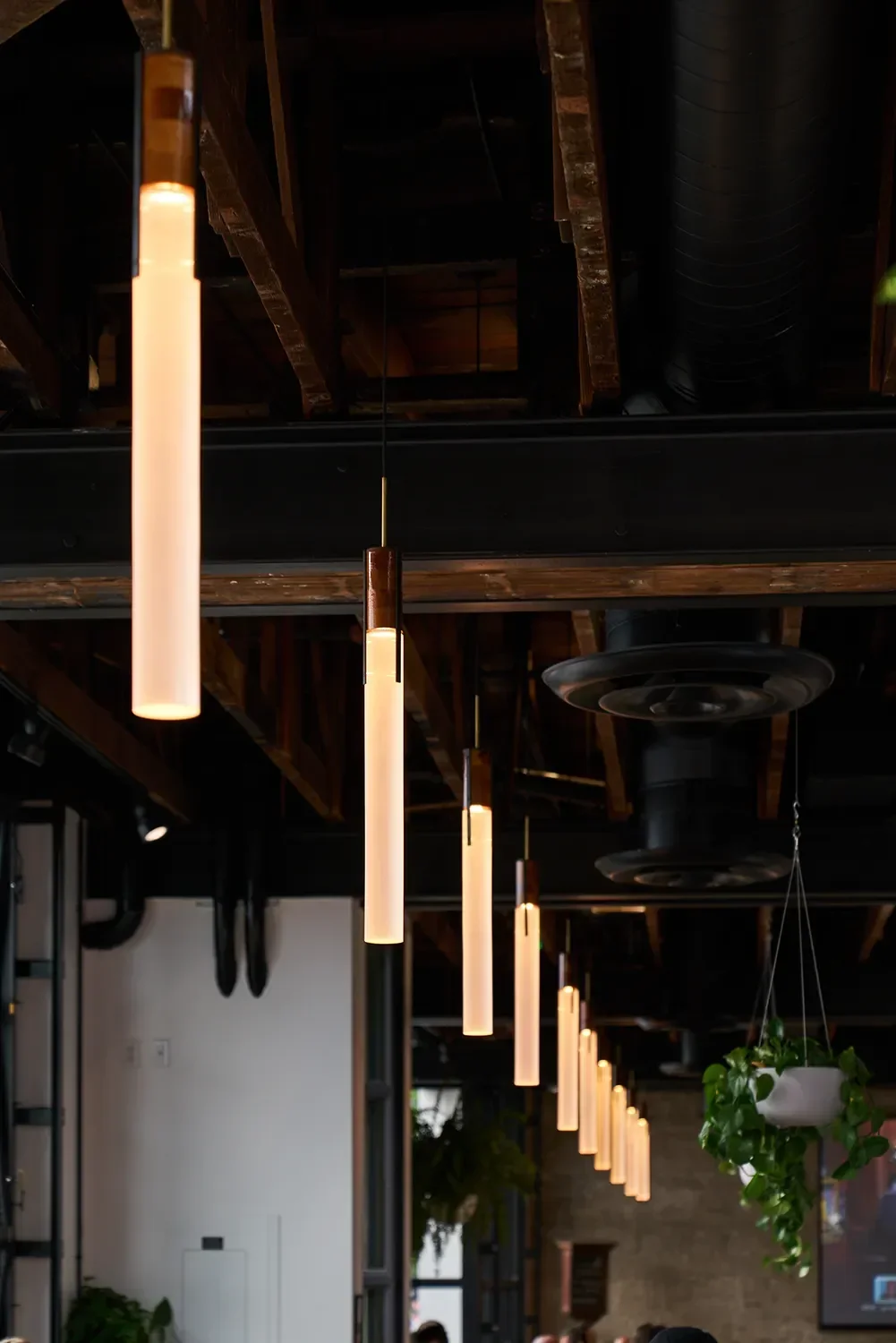 Row of slender illuminated acrylic tube pendants above the bar at Nolita Hall in Little Italy San Diego