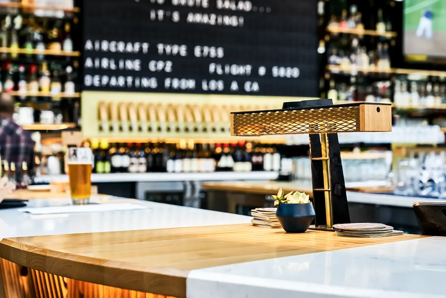 Brass bar lamp on a wood and stone counter with the back bar and menu board behind it, Nolita Hall Little Italy