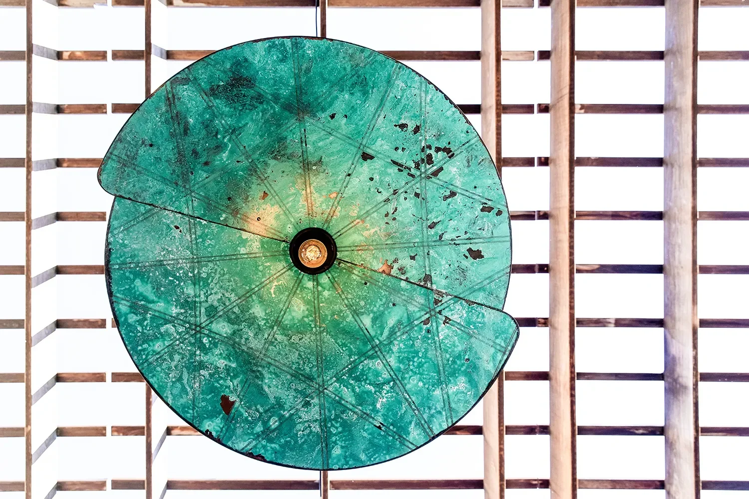 Patinated metal disc pendant light fixtures mounted on a slatted wood patio ceiling