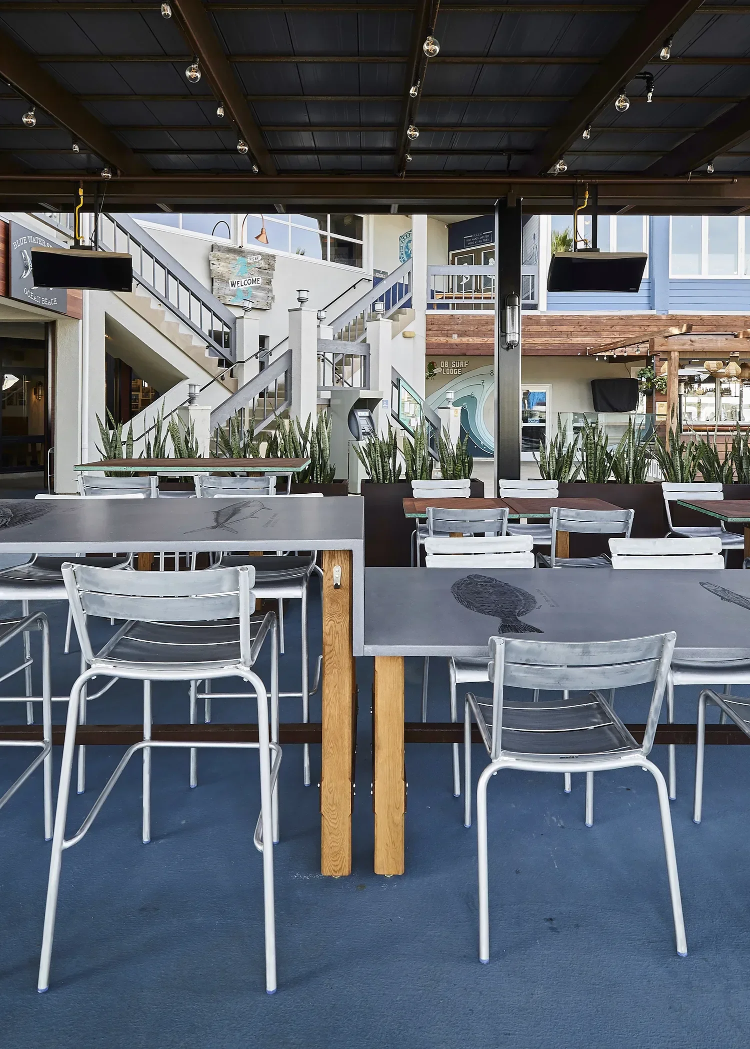 Blue Water Ocean Beach covered patio dining area with custom concrete tables with printed graphics under a canopy structure