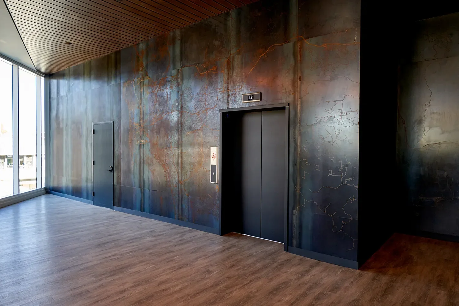 Corten wall cladding feature with acid etched map detail cladding an elevator in a lobby space with wood flooring