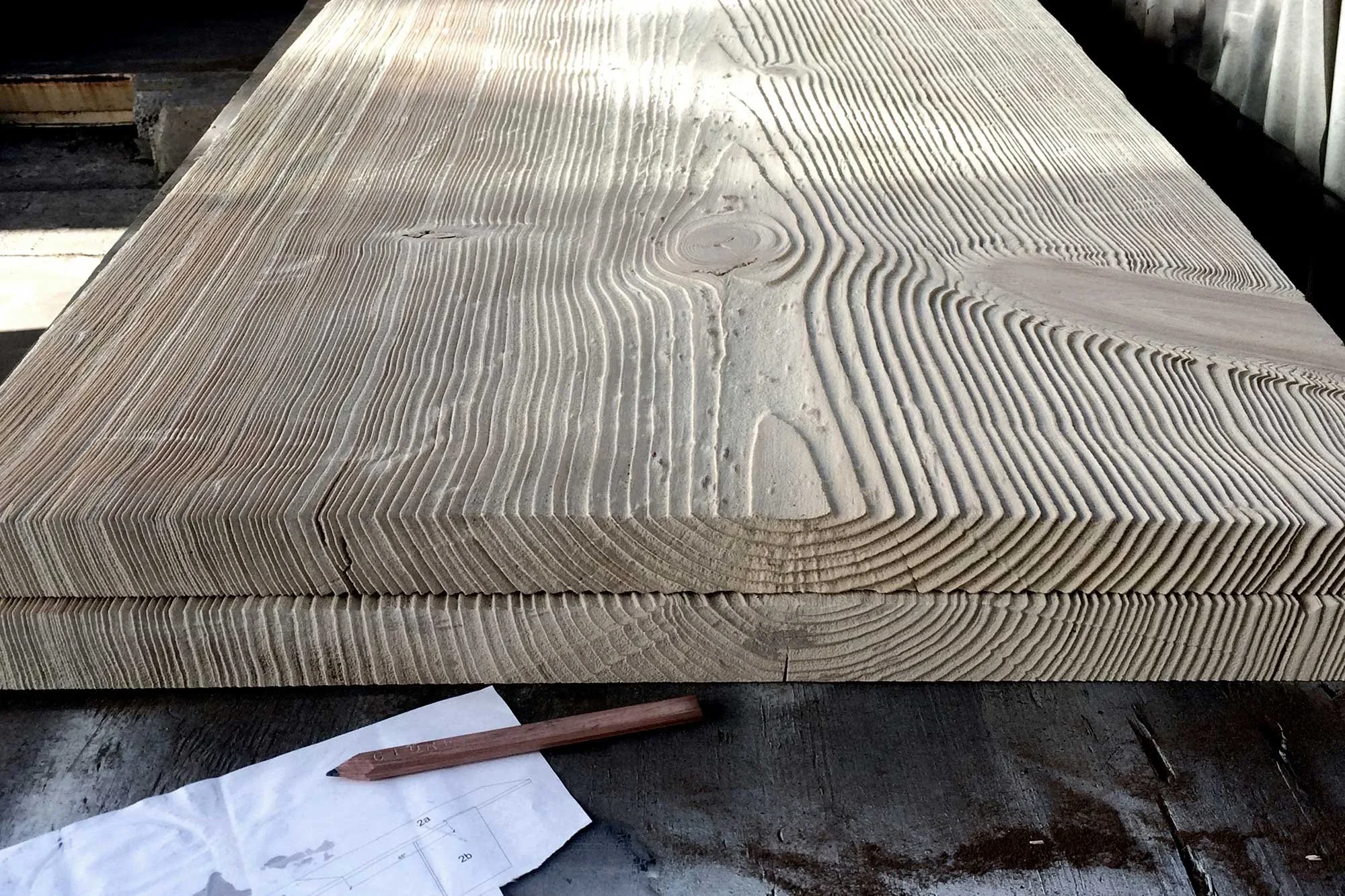 Stack of laminated wood slabs with finely routed lines sitting beside a shop drawing