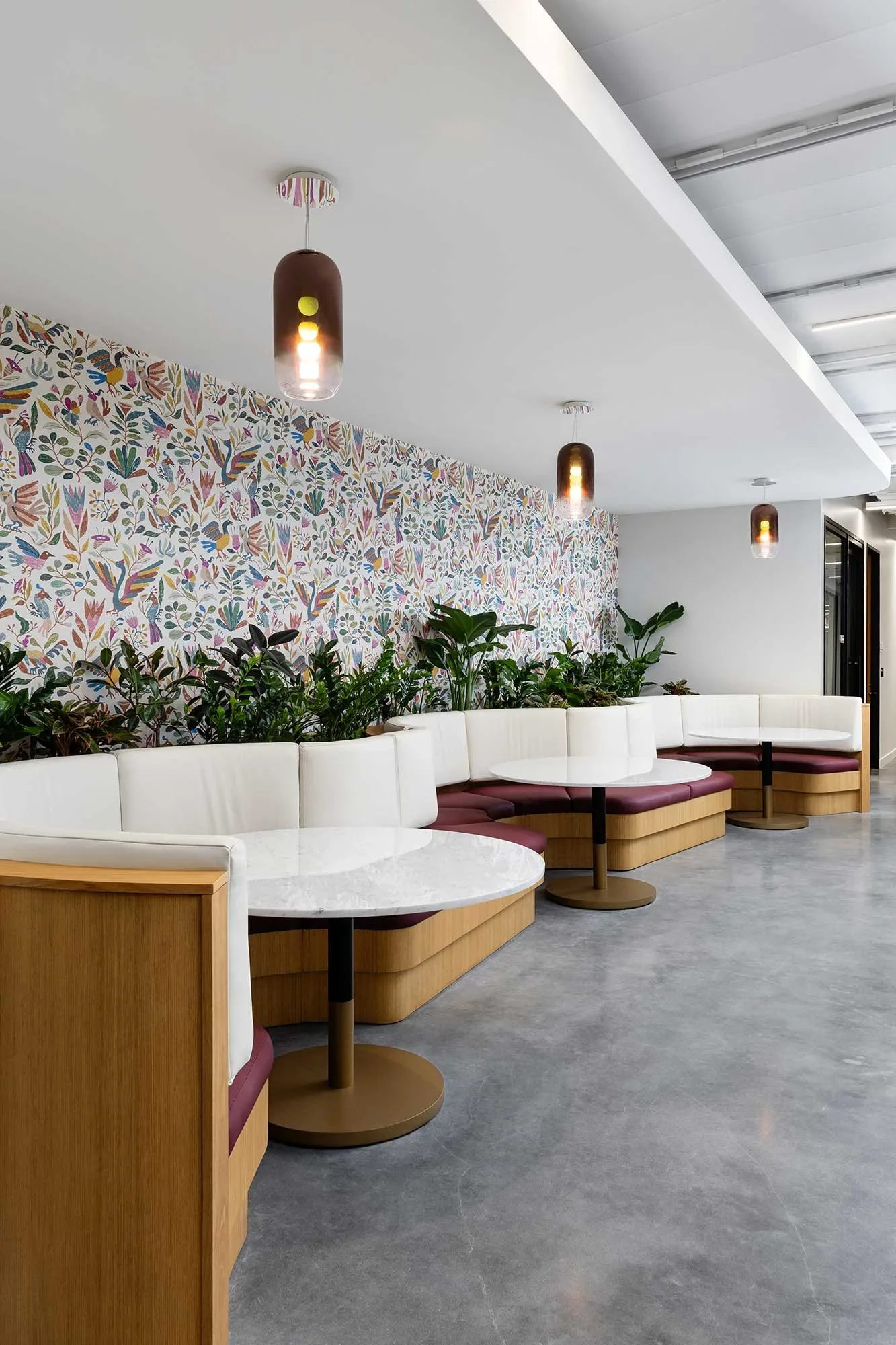 Curved banquette seating and round tables against a patterned wallpaper feature wall at a Corporate Office Interior in San Diego
