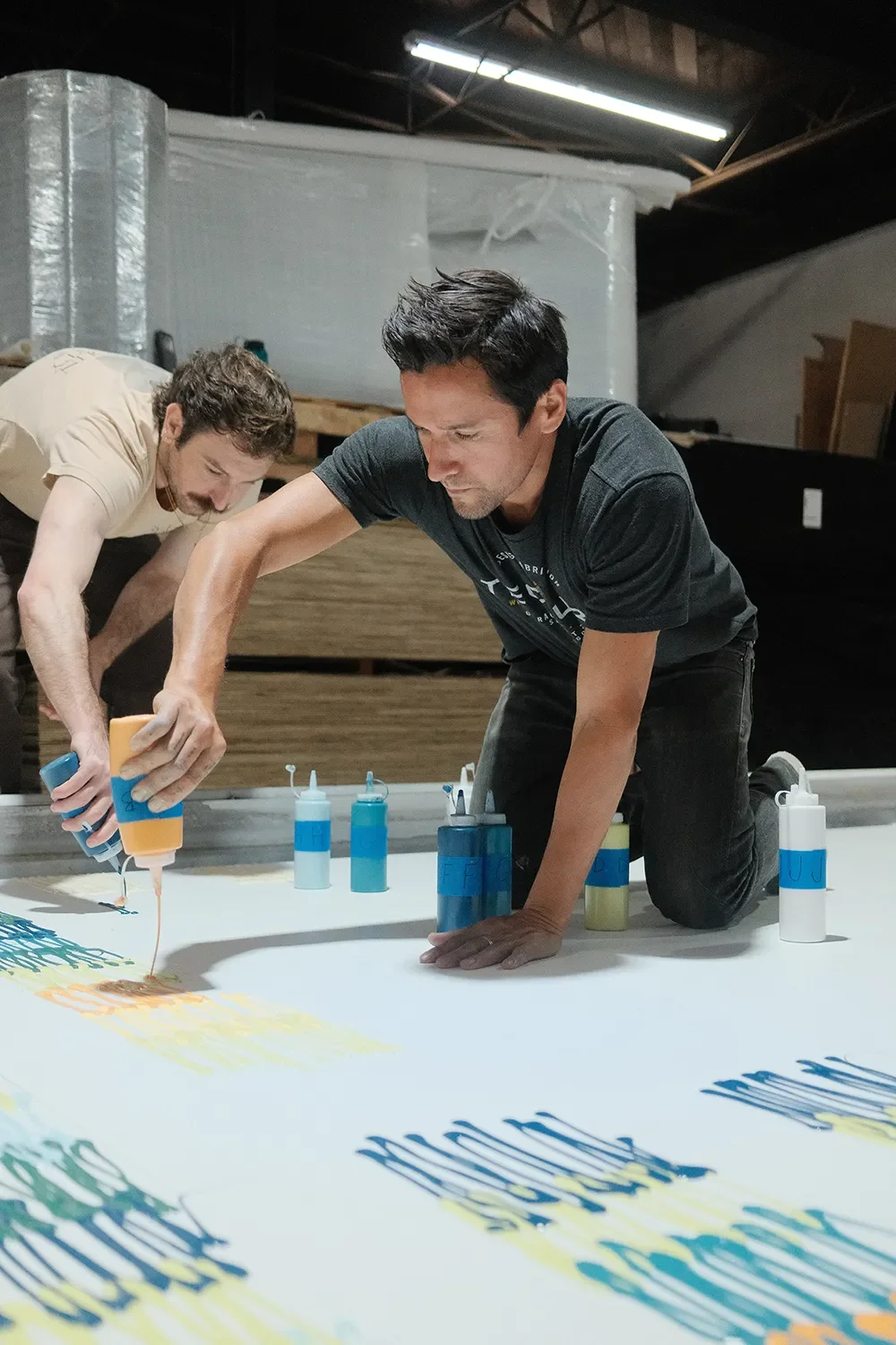 Two Tecture crew members layout out colors on a panel with lettered paint bottles