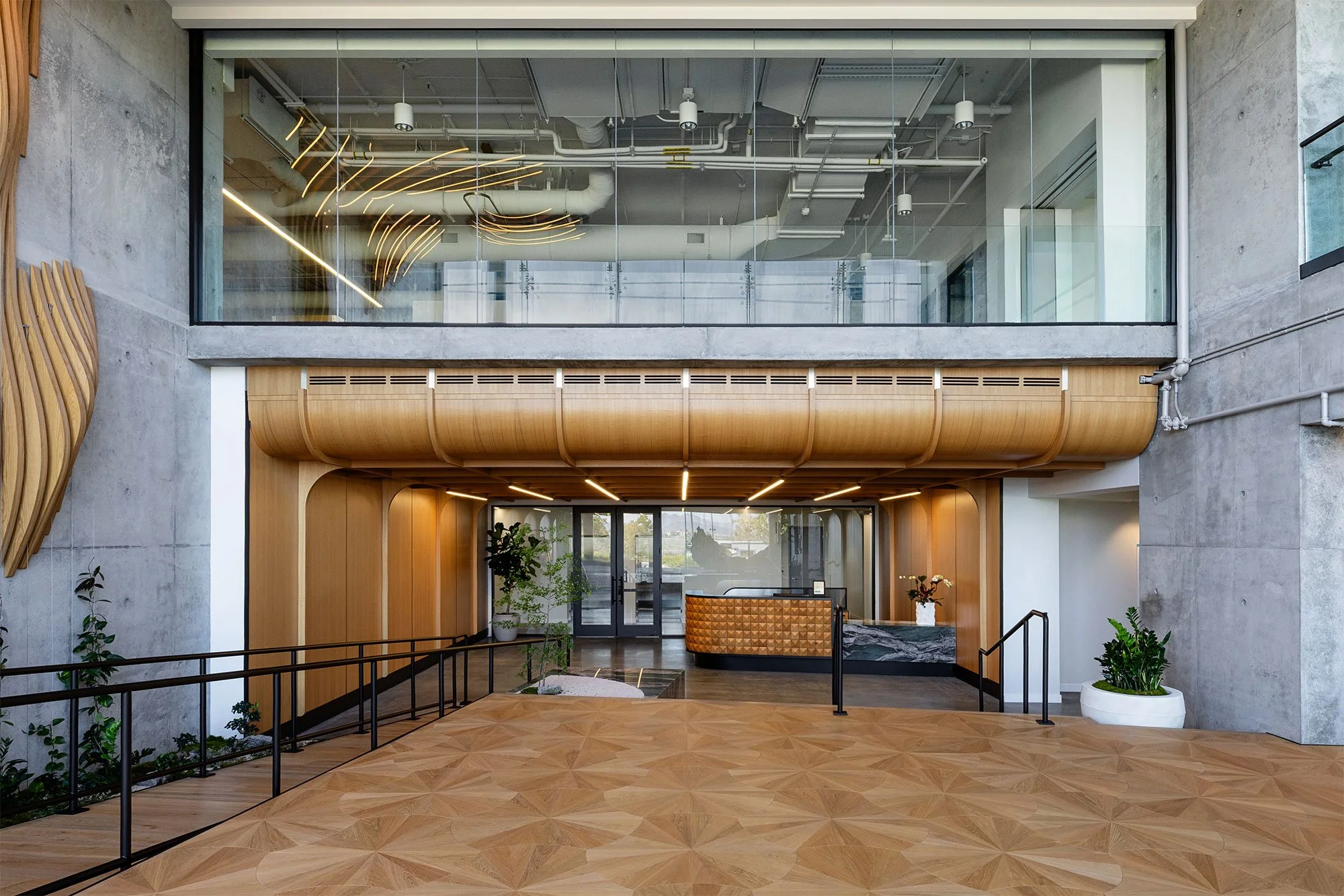 Double-height Corporate Office lobby with a custom wood ceiling, sculptural millwork, custom fabricated reception desk, and reflection of the Parametric Wall in the glass above