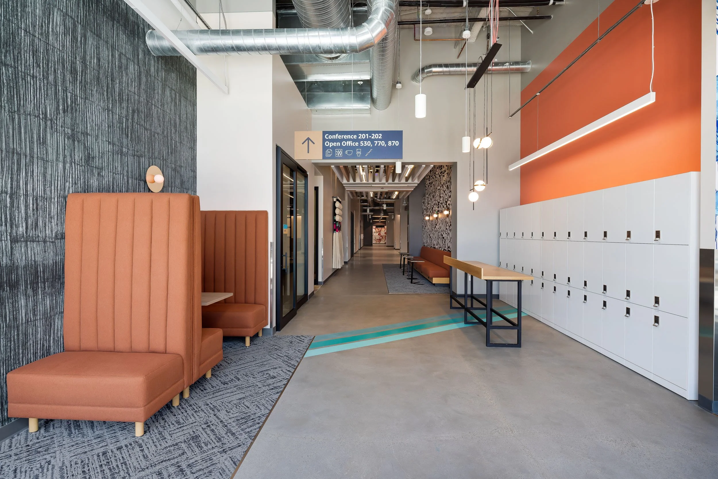 Custom floor graphic leading to orange booth seating across from an orange wall with lockers, at a corporate office building.