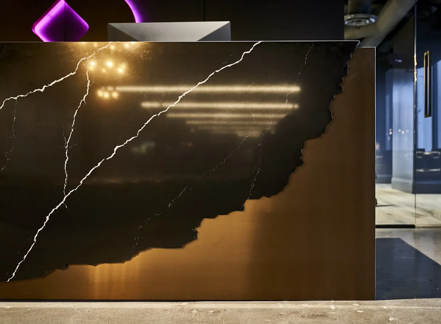 Back marble stone with serrated edges, over brass metalwork reception desk in the Smashtech lobby, San Diego California