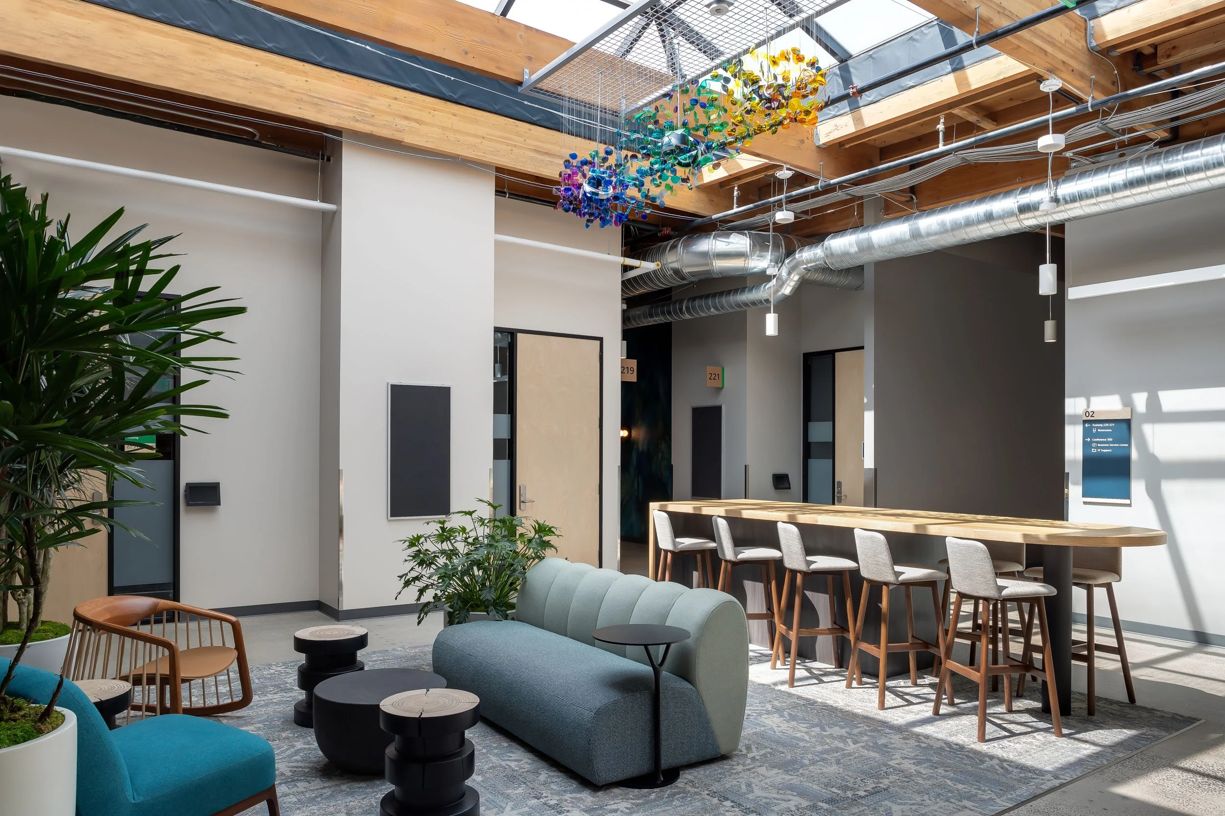 A corporate office lounge space with a lounge area and counter-height seating, underneath a glass ceiling with a custom suspended colored sculpture.