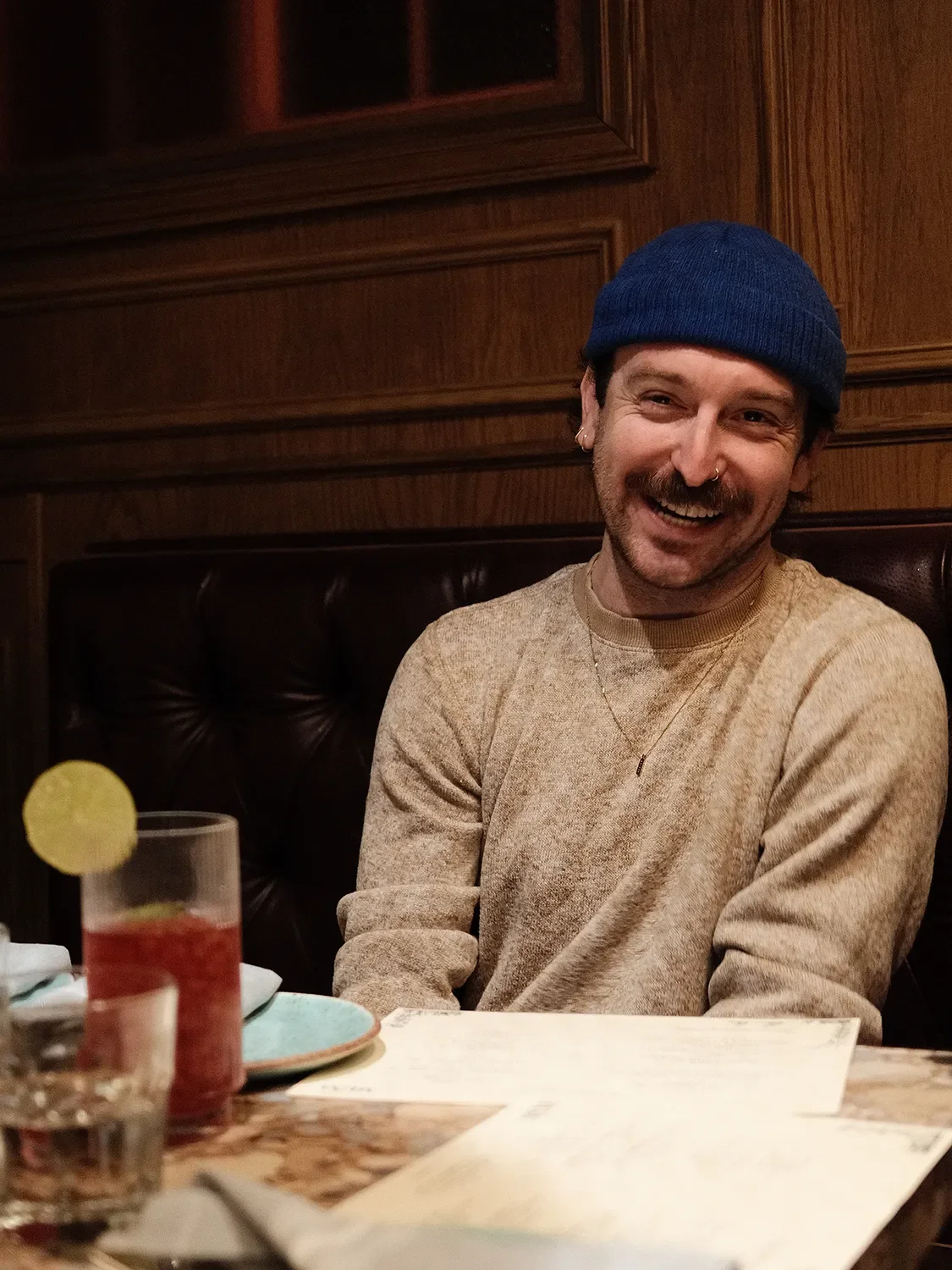 Jonny Hoolko smiling and laughing while on a design tour with the Tecture Studio team at a restaurant table with drinks and menus