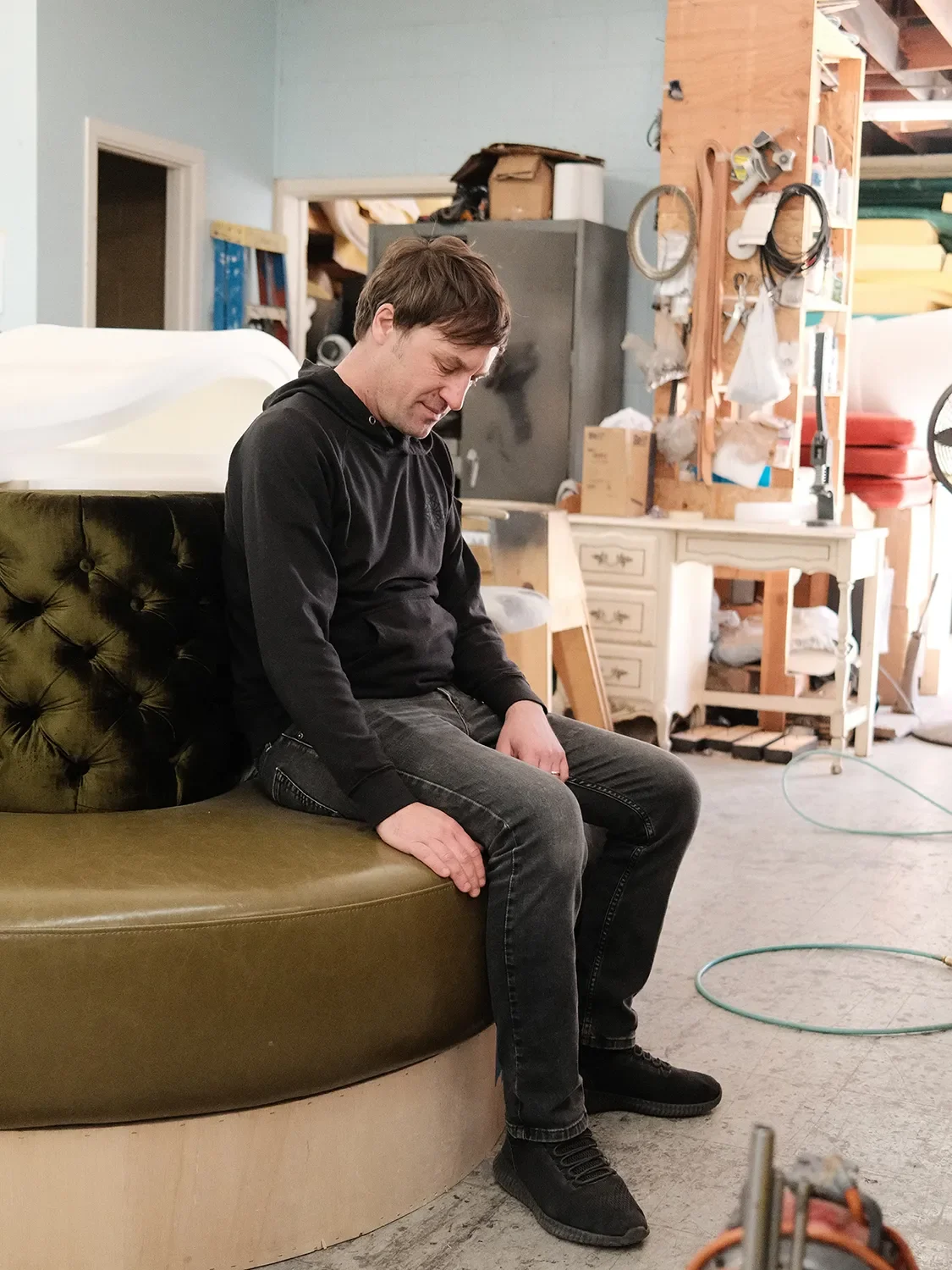 Alex Brewins sitting on a custom curved banquette with green upholstery and a wood base in the Tecture shop