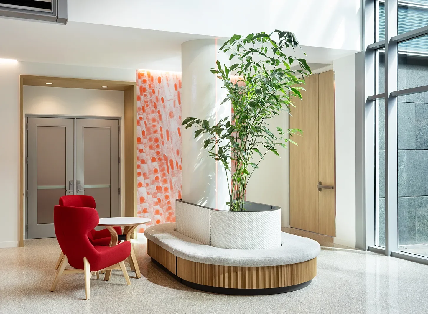 Curved wood-clad bench and planter with a red lounge chair in the Johnson & Johnson lobby in Torrey Pines