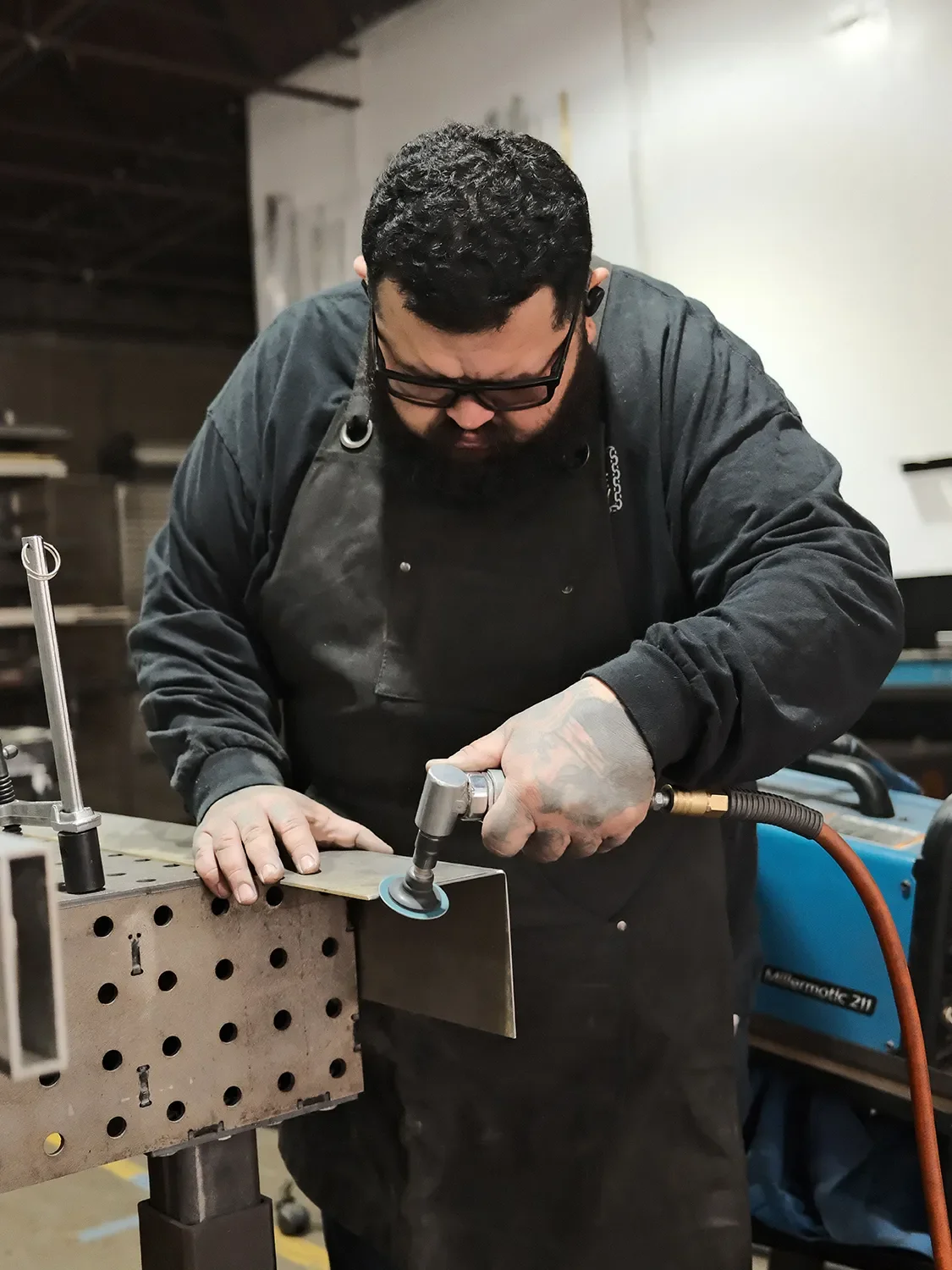 Ernesto Sanchez using a handheld grinder to finish a metal component clamped to a fabrication table