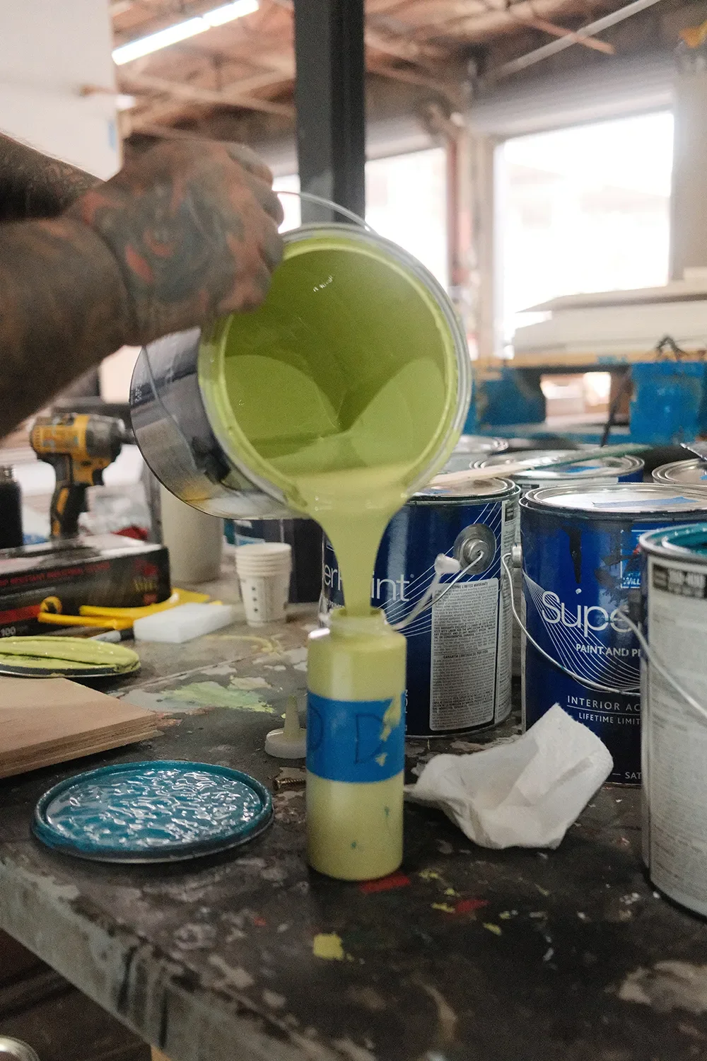Light green paint being poured into a bottle while mixing colors for the Convergence wall art installation