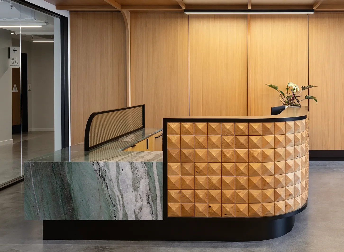 Custom reception desk with a faceted wood front and stone counter in a San Diego corporate lobby