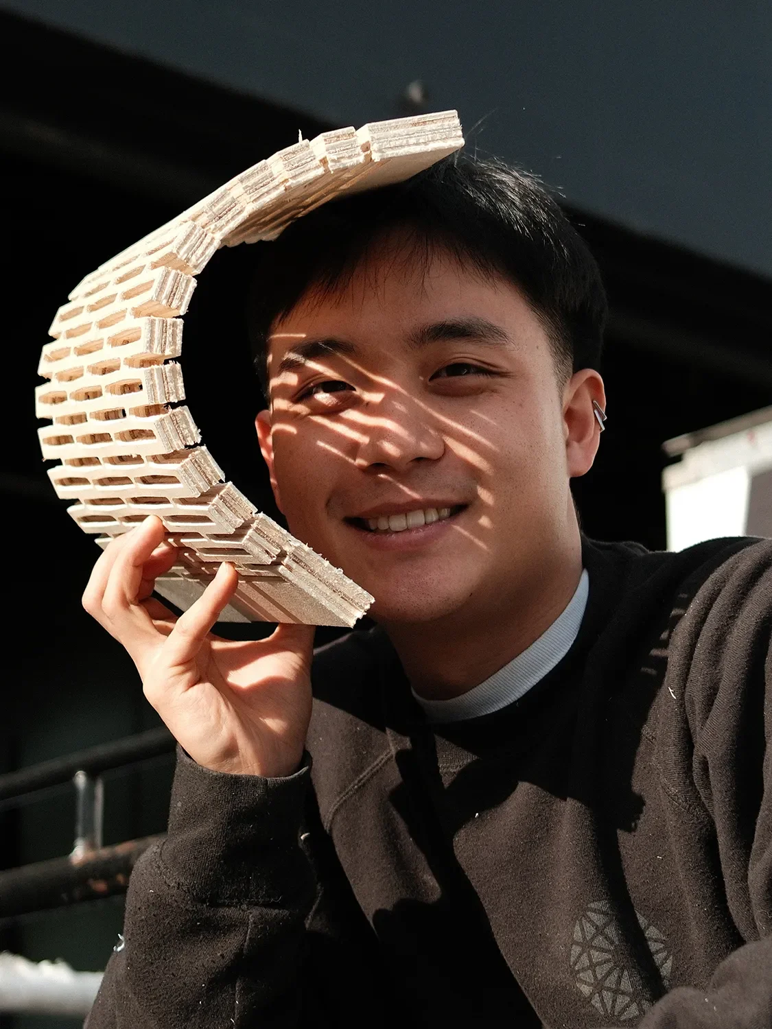 Matias Lee holding a curved, slotted wood sample that casts patterned shadow across his face