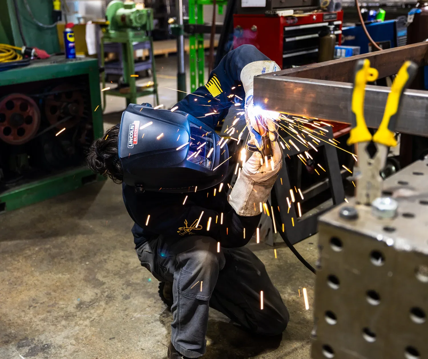 Fabricator welding a metal assembly in the Tecture AF shop with protective face gear and metal sparks