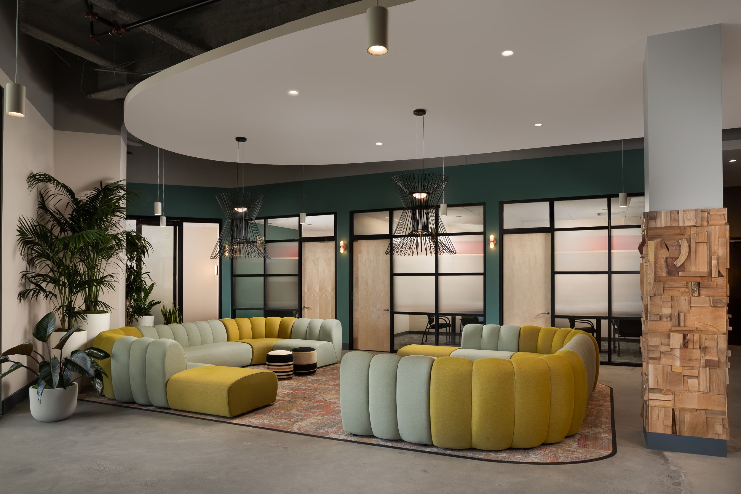 An open office lounge space with a curved dropped ceiling and a curved yellow and light blue modular sofa.