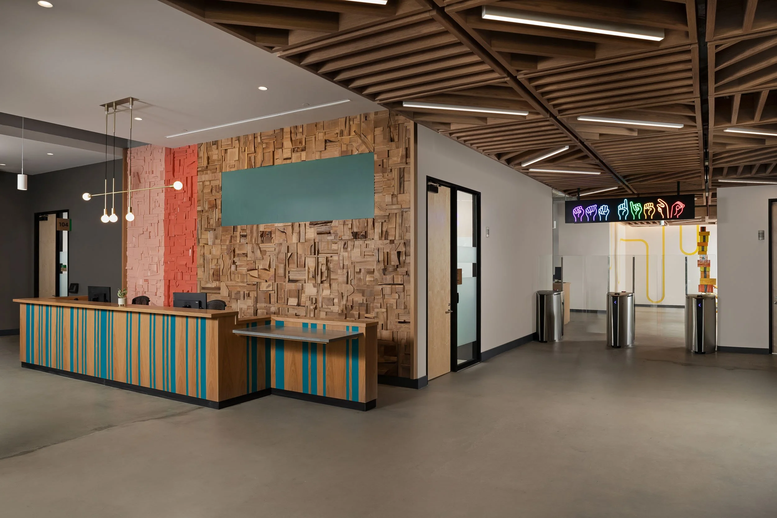 A custom wood reception desk with painted blue stripes in front of a wooden feature wall, and a custom hanging neon sign with hand signal icons.