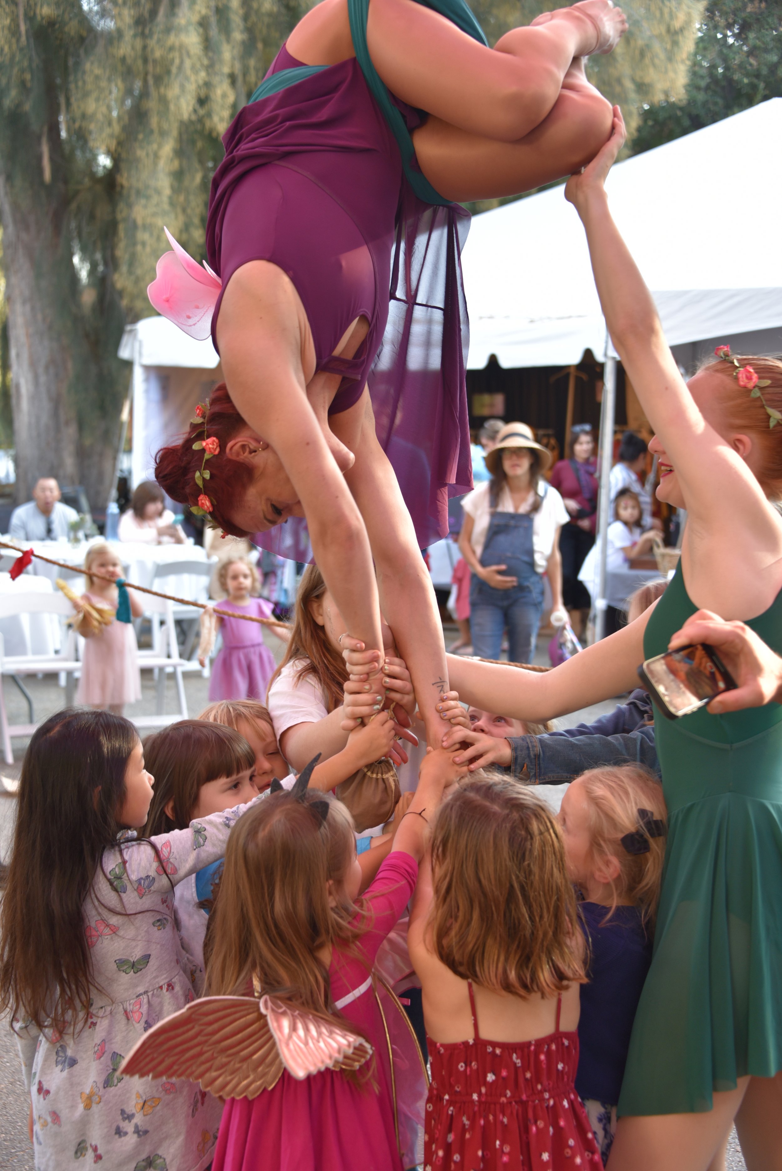 Circus performer doing an aerial act supported by kids at an outdoor event.