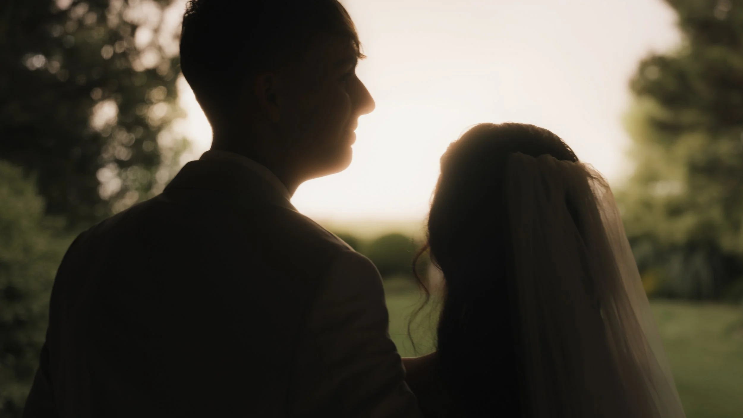 Silhouette of a man and woman close together outdoors at sunset, with trees and sunlight in the background.