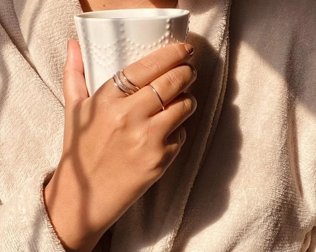 A person holding a white mug with a textured heart pattern, wearing rings on their fingers, and dressed in a soft beige or cream jacket. Features a preview of Dr. Troy Rohn's book 'Brain Medicine.'